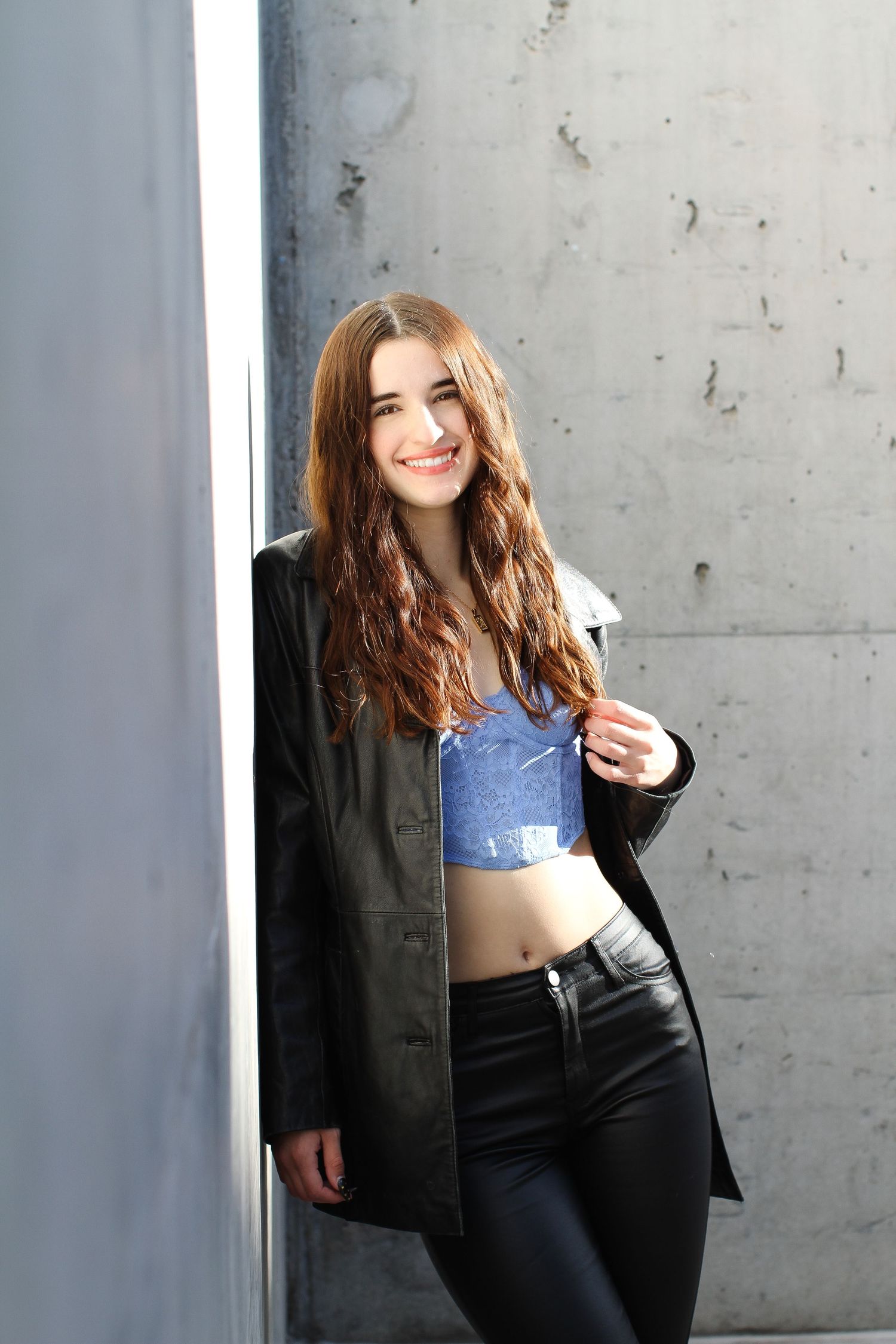 Fashion portrait of a model in black blazer and crop top against concrete wall.