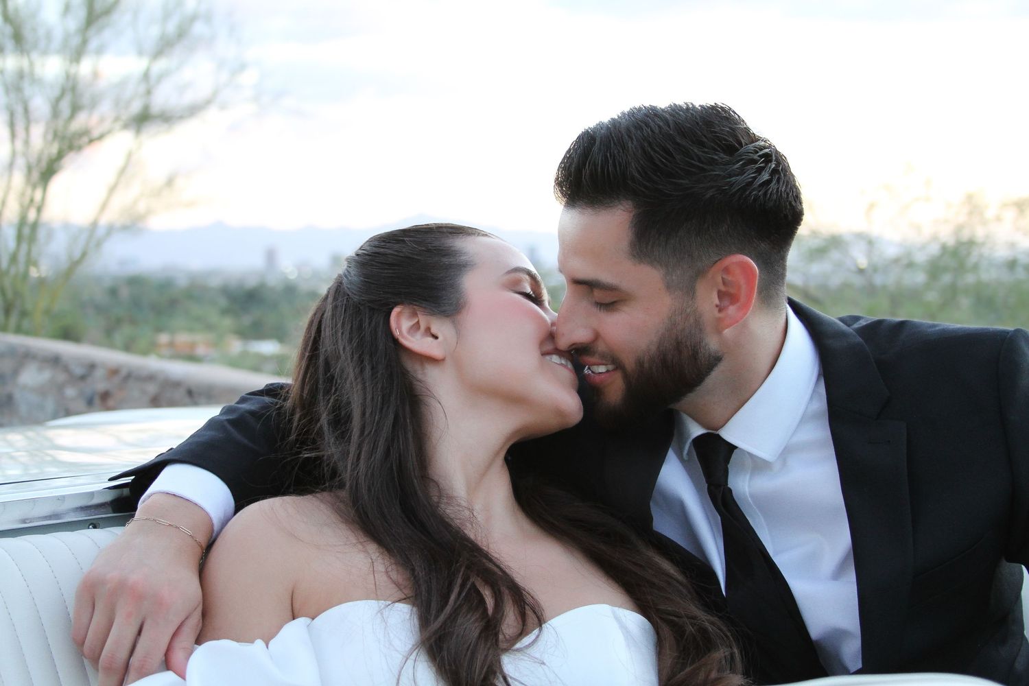 A romantic couple shares a tender moment while dressed in formal wedding attire against a scenic outdoor backdrop.