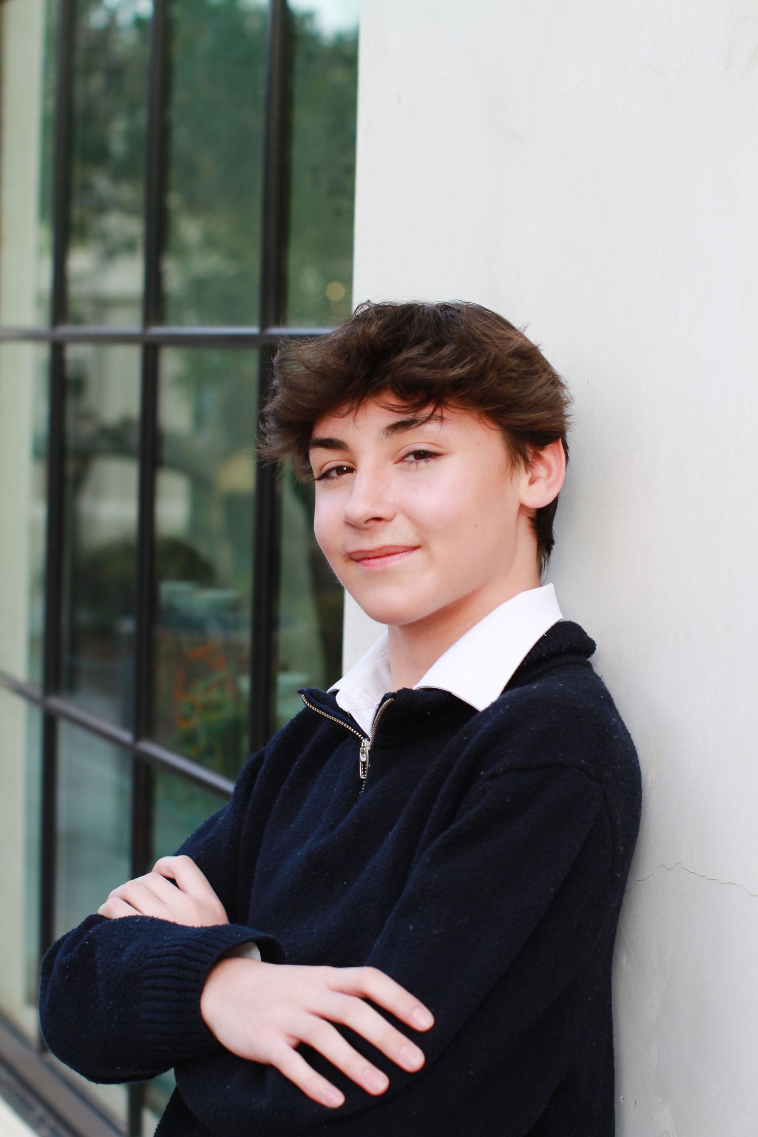 Portrait against white wall wearing navy sweater and white collared shirt.