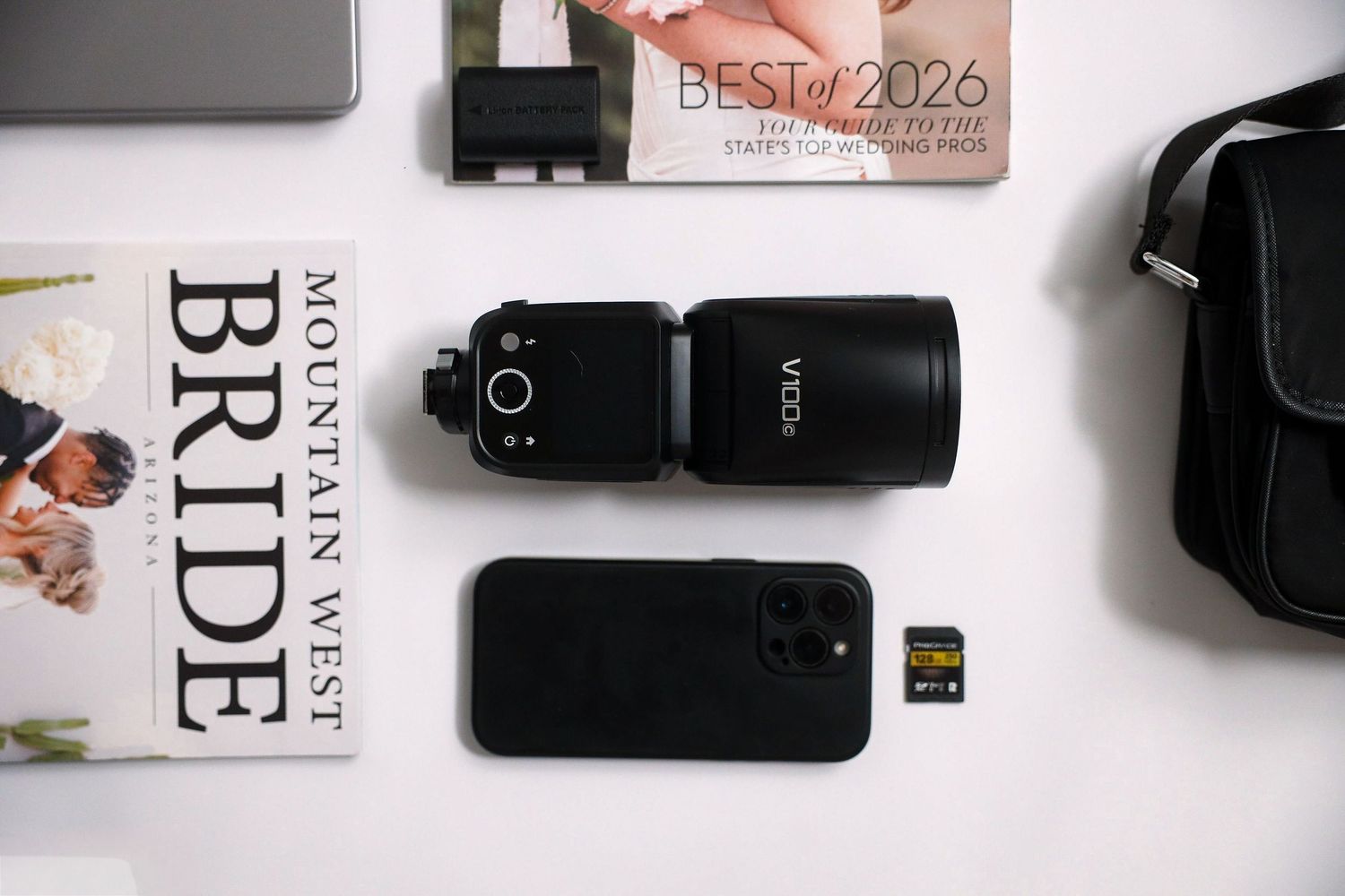 Flat lay of wedding photography gear including a camera flash, smartphone, SD card, and Bride magazine.