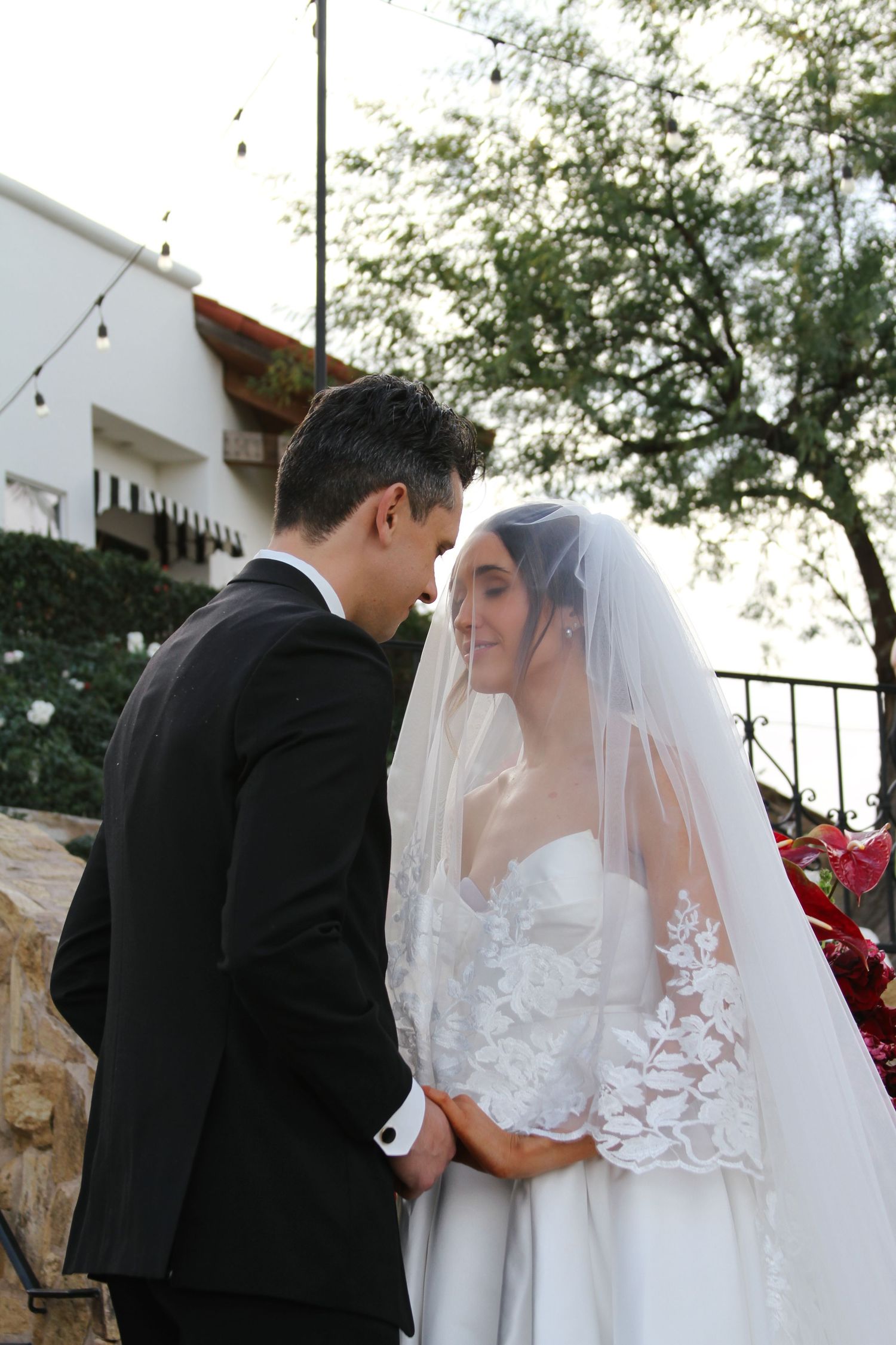 Bride and groom share an intimate moment at outdoor wedding ceremony, bride wearing lace veil and white gown.