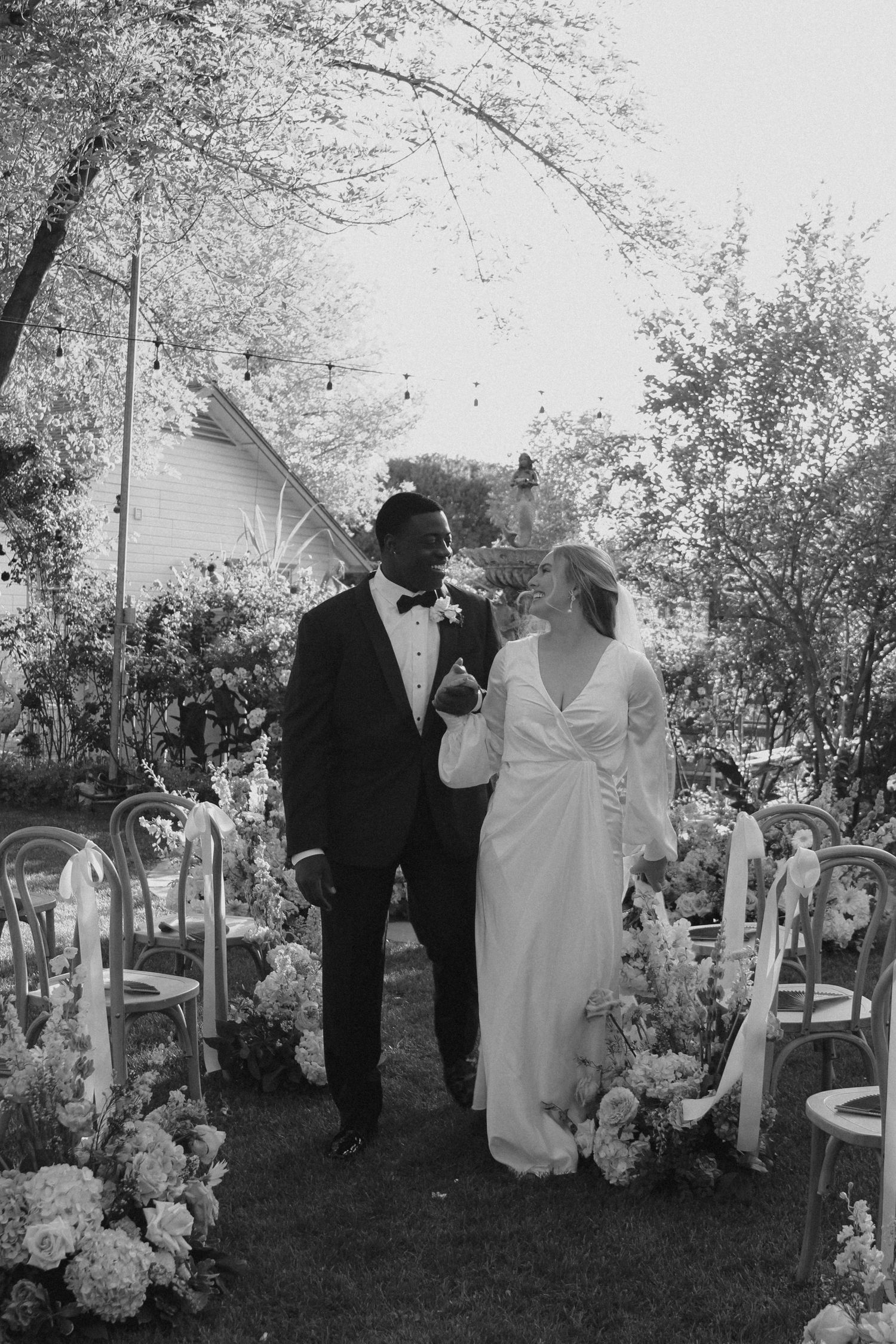 A black and white photo of a romantic outdoor garden wedding ceremony with elegant floral arrangements and white chairs.