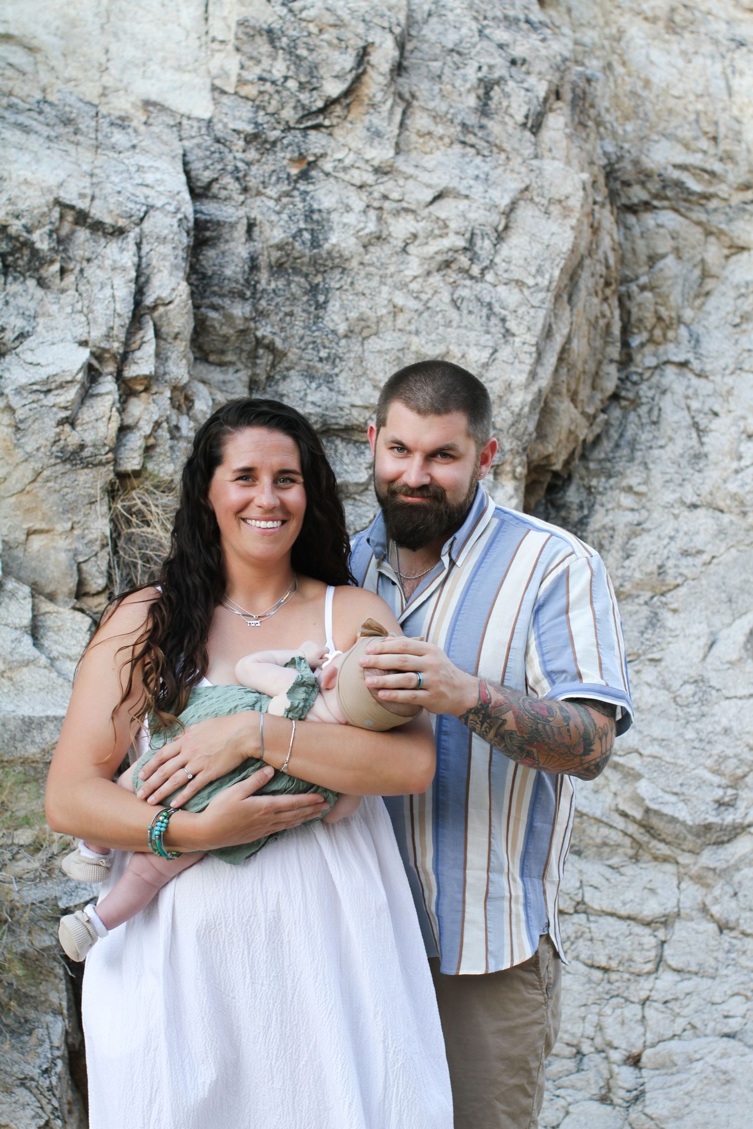 A couple poses together against a rocky wall background outdoors.
