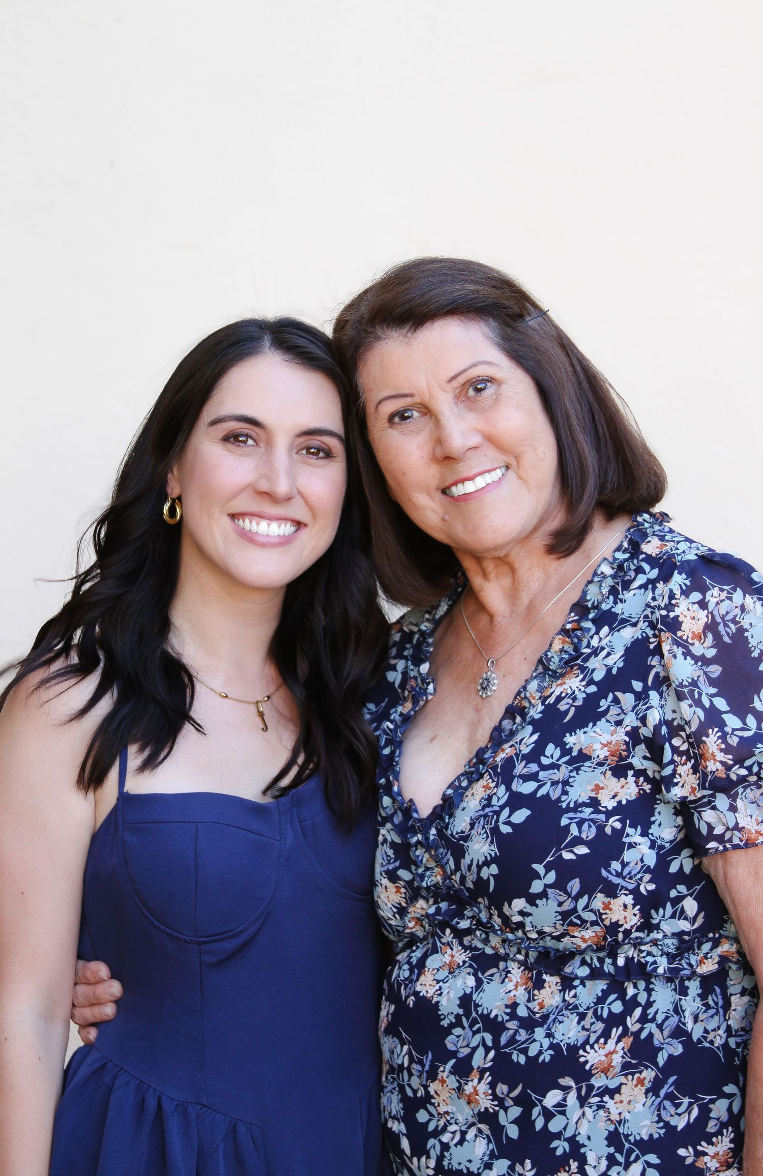 Two people in blue and floral dresses posing together against white background.