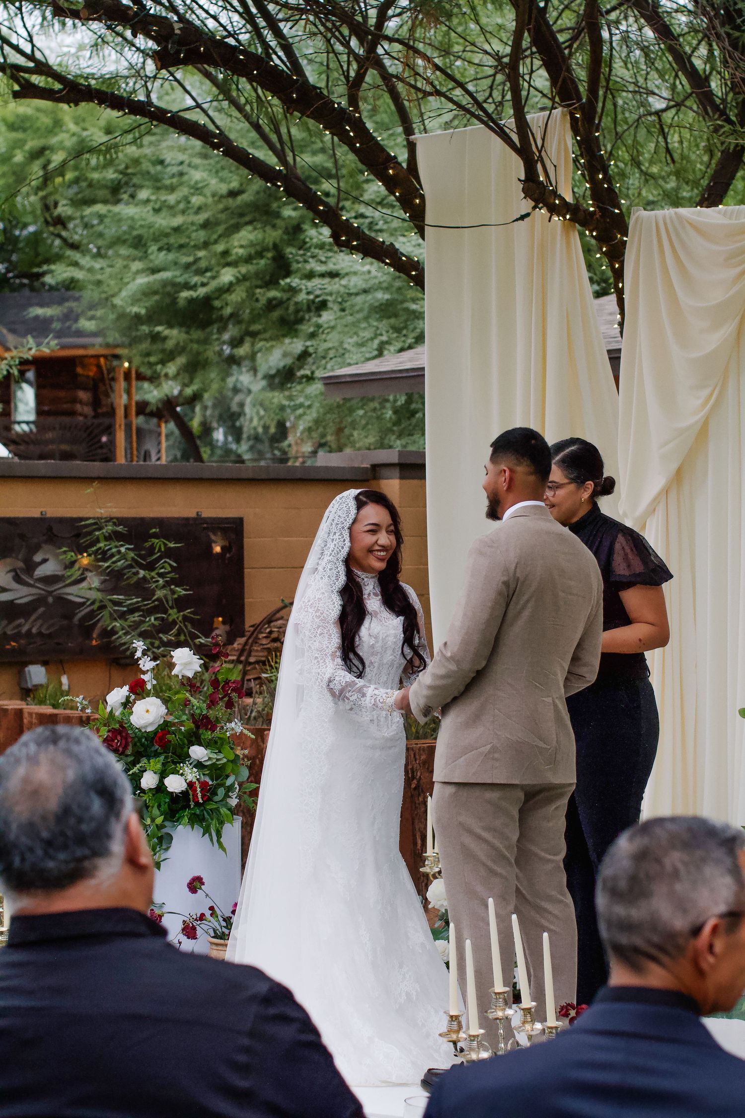 A wedding ceremony takes place outdoors under white draping with floral arrangements and guests in attendance. Tyler Garlej Photography