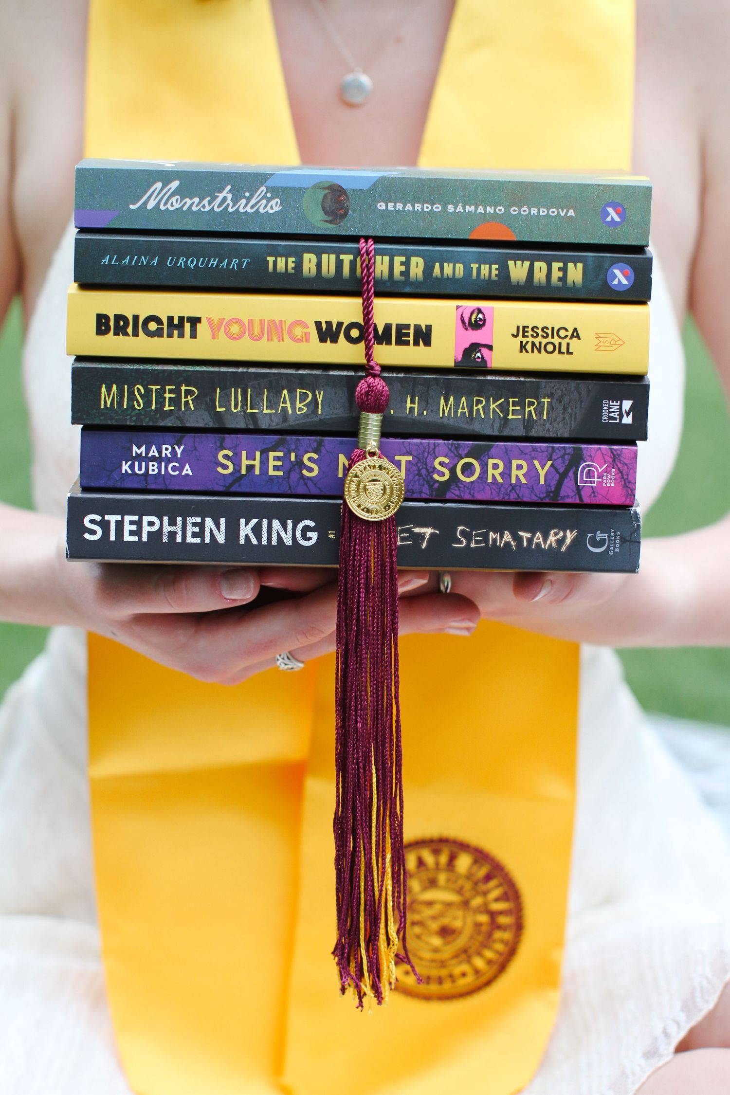 Stack of books with graduation tassel against yellow graduation stole.