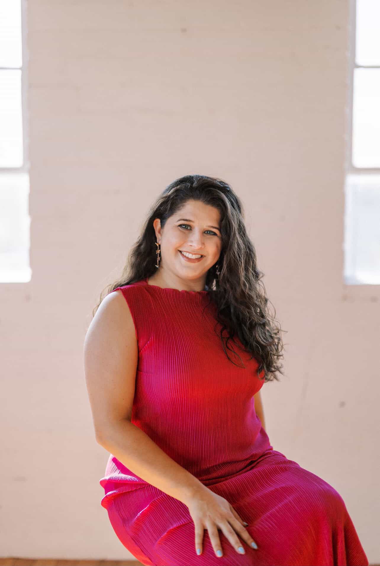 Tyler Garlej Photography - A person in a vibrant red dress poses gracefully in front of a light-colored wall with windows.