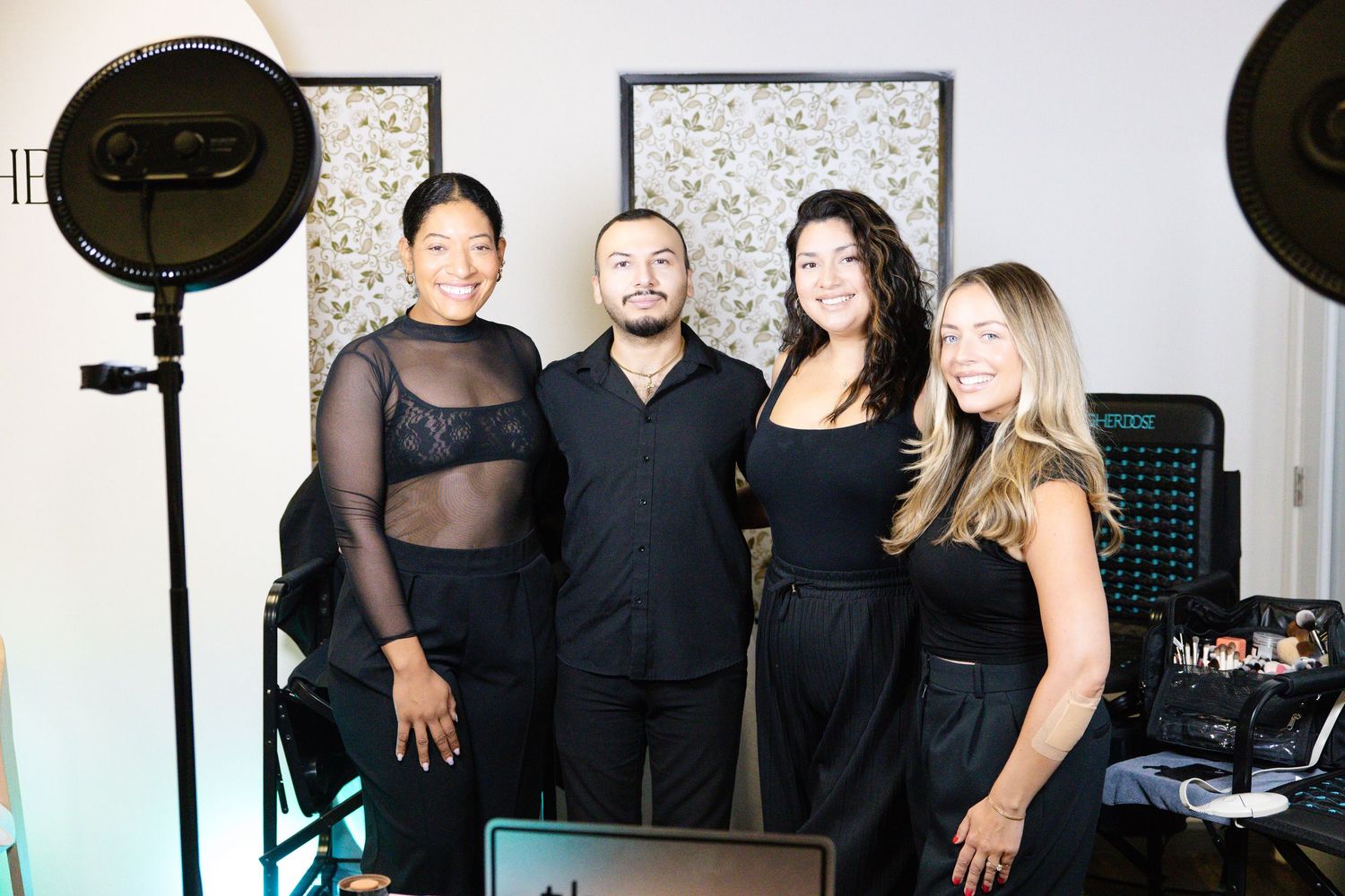 Four people in black attire smile together at a professional photo studio event with ring lights.