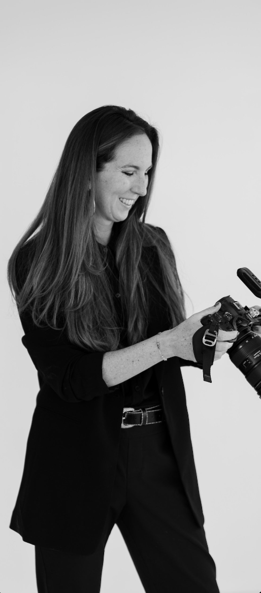 Professional photographer in black outfit examining camera equipment against white background.