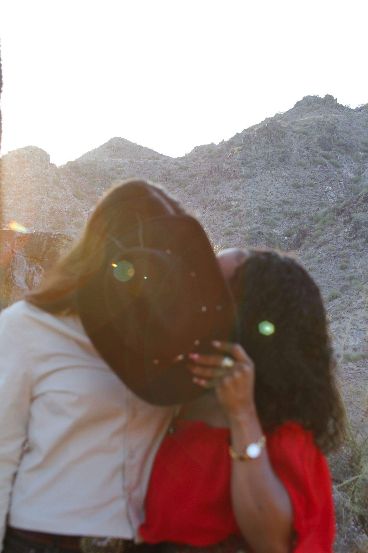 Two people in front of mountain landscape at sunset with lens flare.