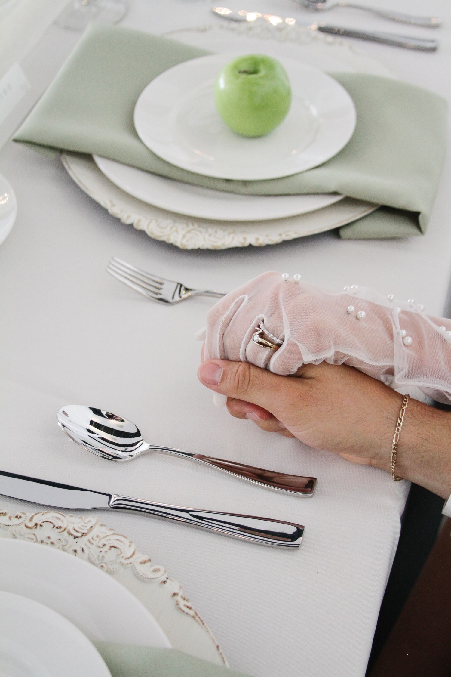 Wedding table setting with green apple place card holder, sage napkin, and silver cutlery on white linen.