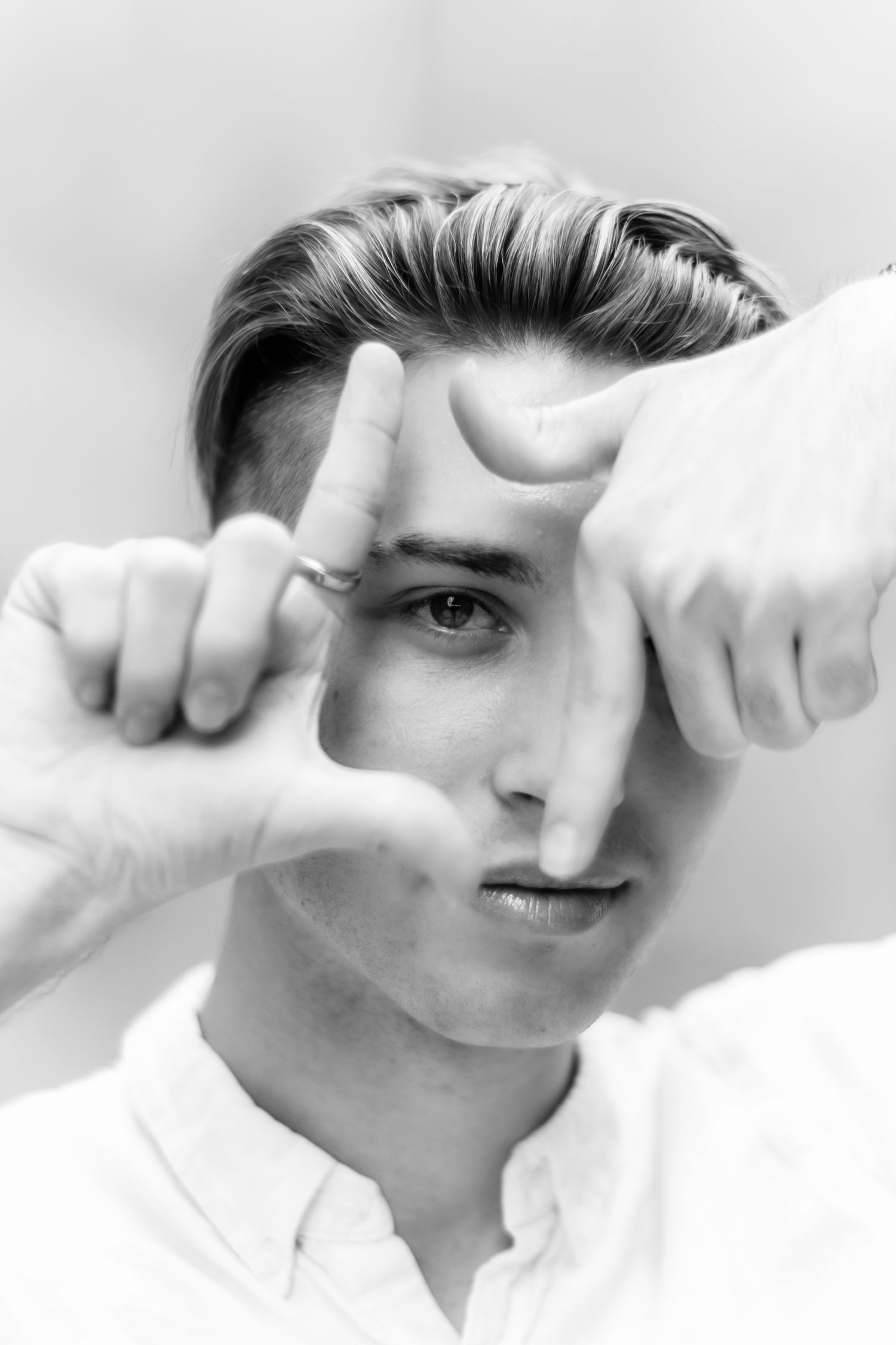 A black and white portrait of a young man framing his face with his hands.