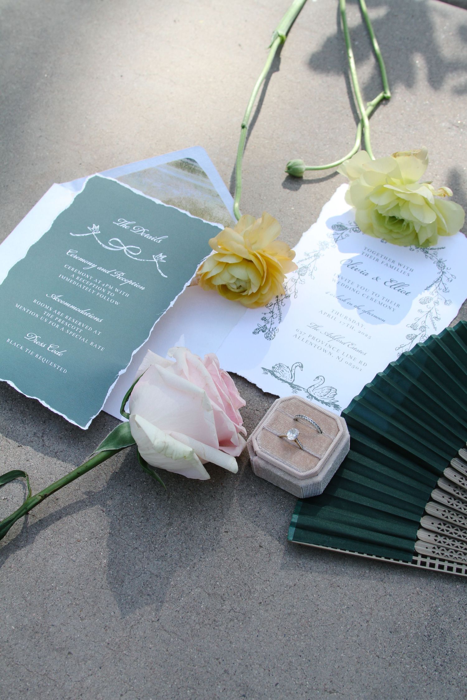 Wedding invitations with delicate floral decorations and green accents displayed on a gray surface. Tyler Garlej Photography