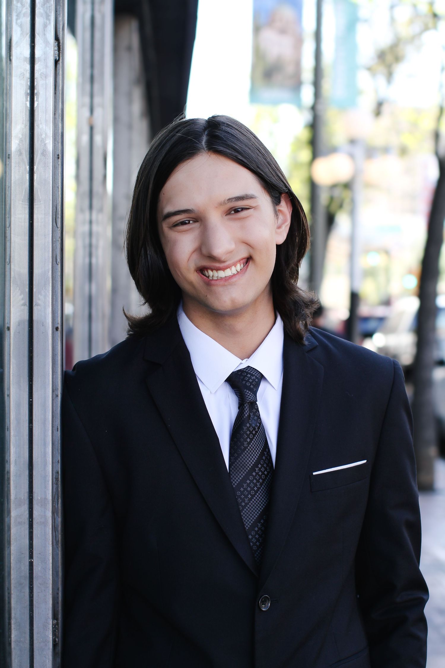 Professional portrait of a business person in a black suit and tie smiling against an urban background.
