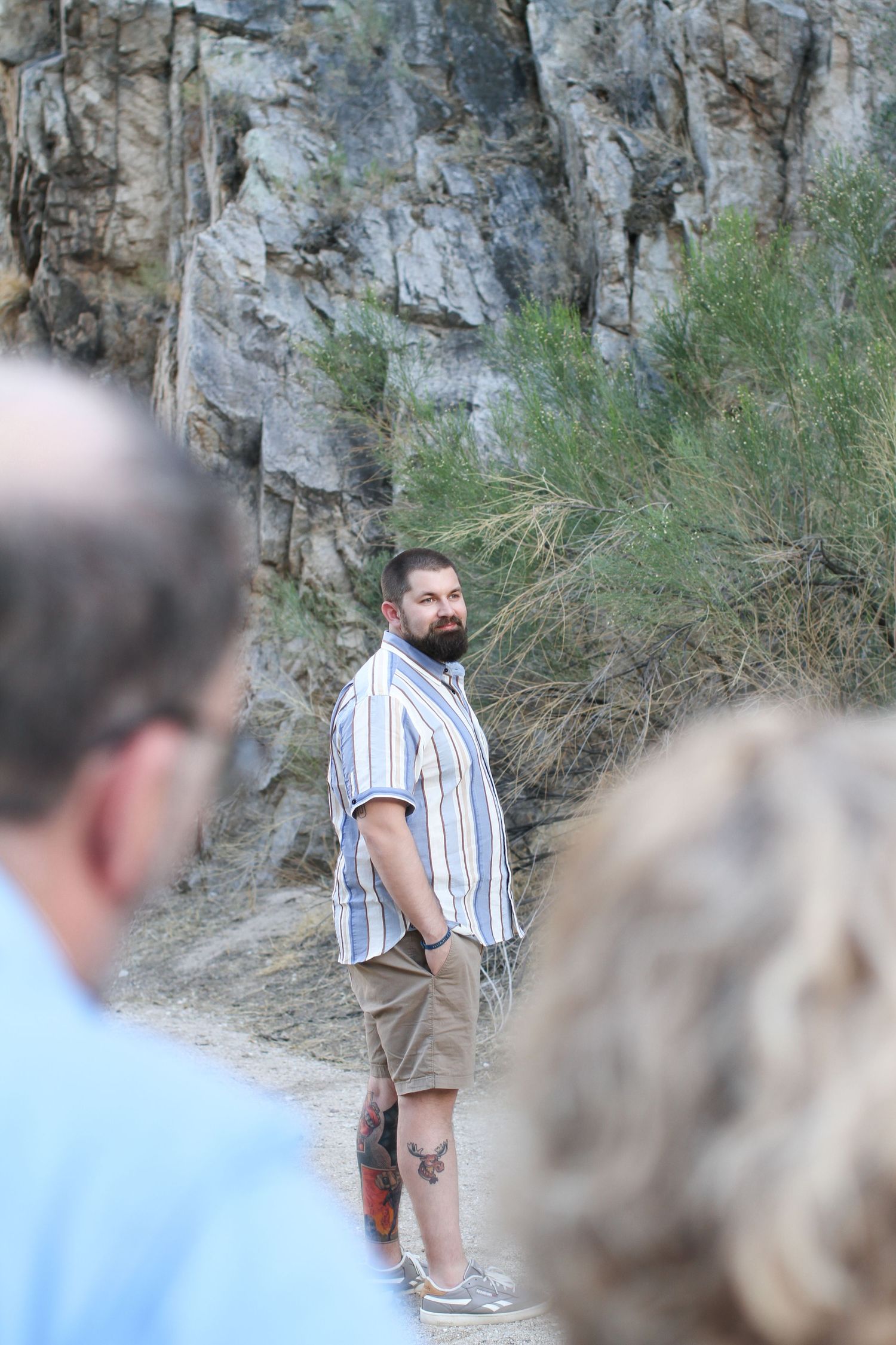 Man in striped shirt and shorts standing against rocky cliff backdrop.