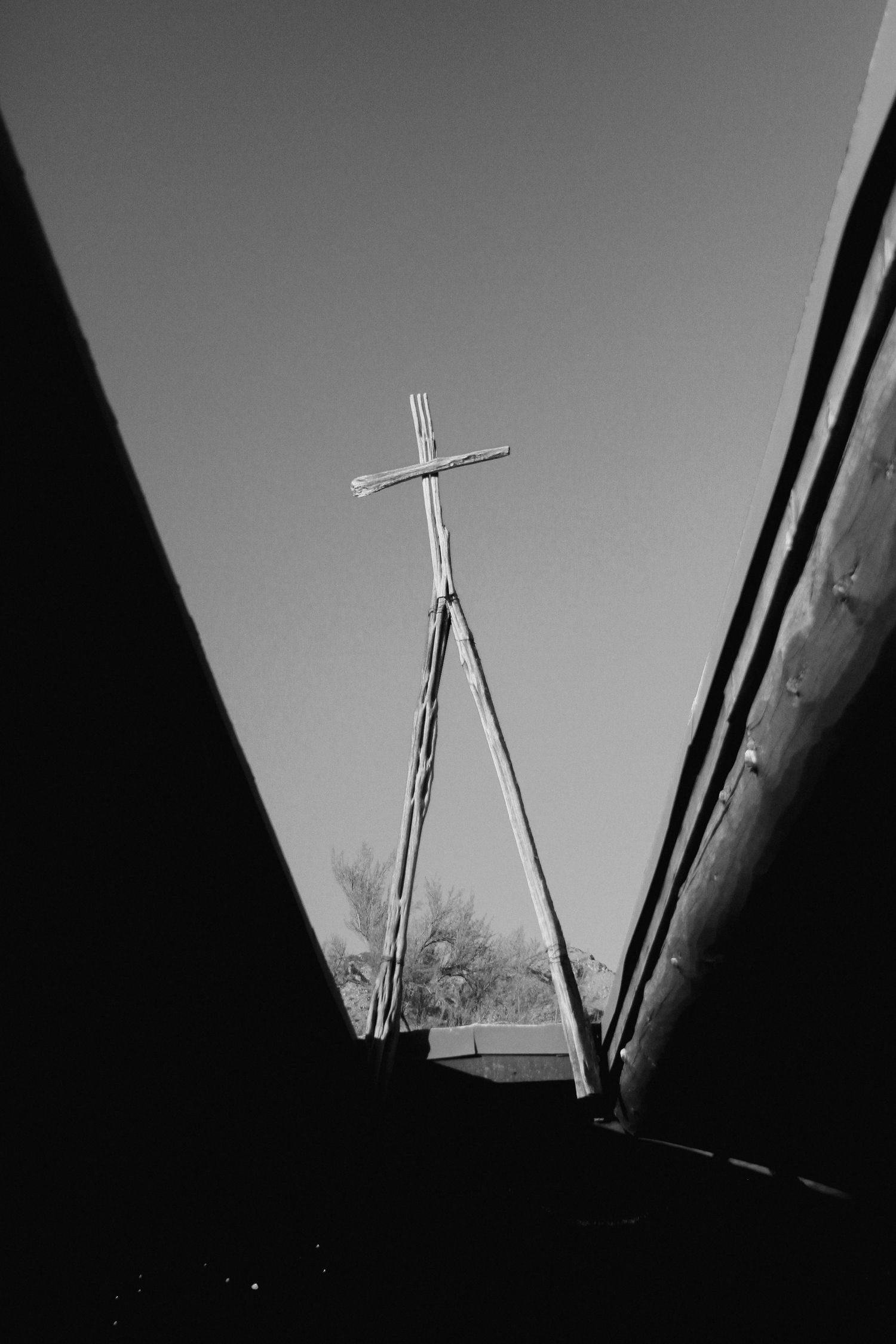 Black and white image of metal cross silhouetted against dramatic sky.