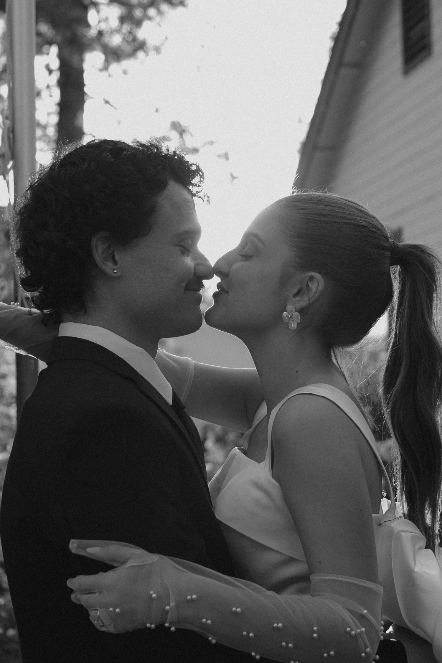 Black and white photo of a bride and groom sharing a romantic kiss outdoors on their wedding day.
