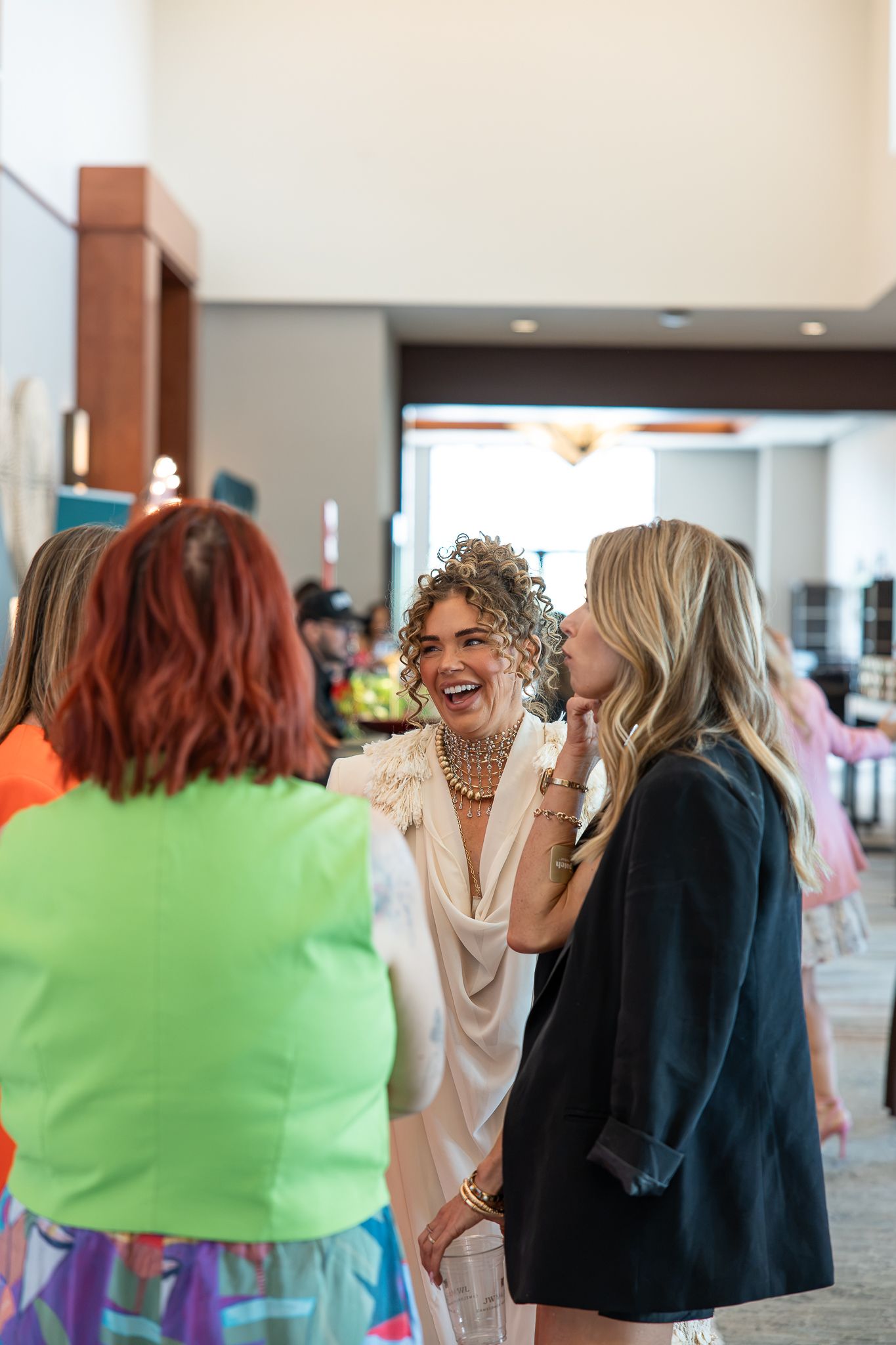 Women in colorful attire laughing and socializing at an indoor event or party gathering.
