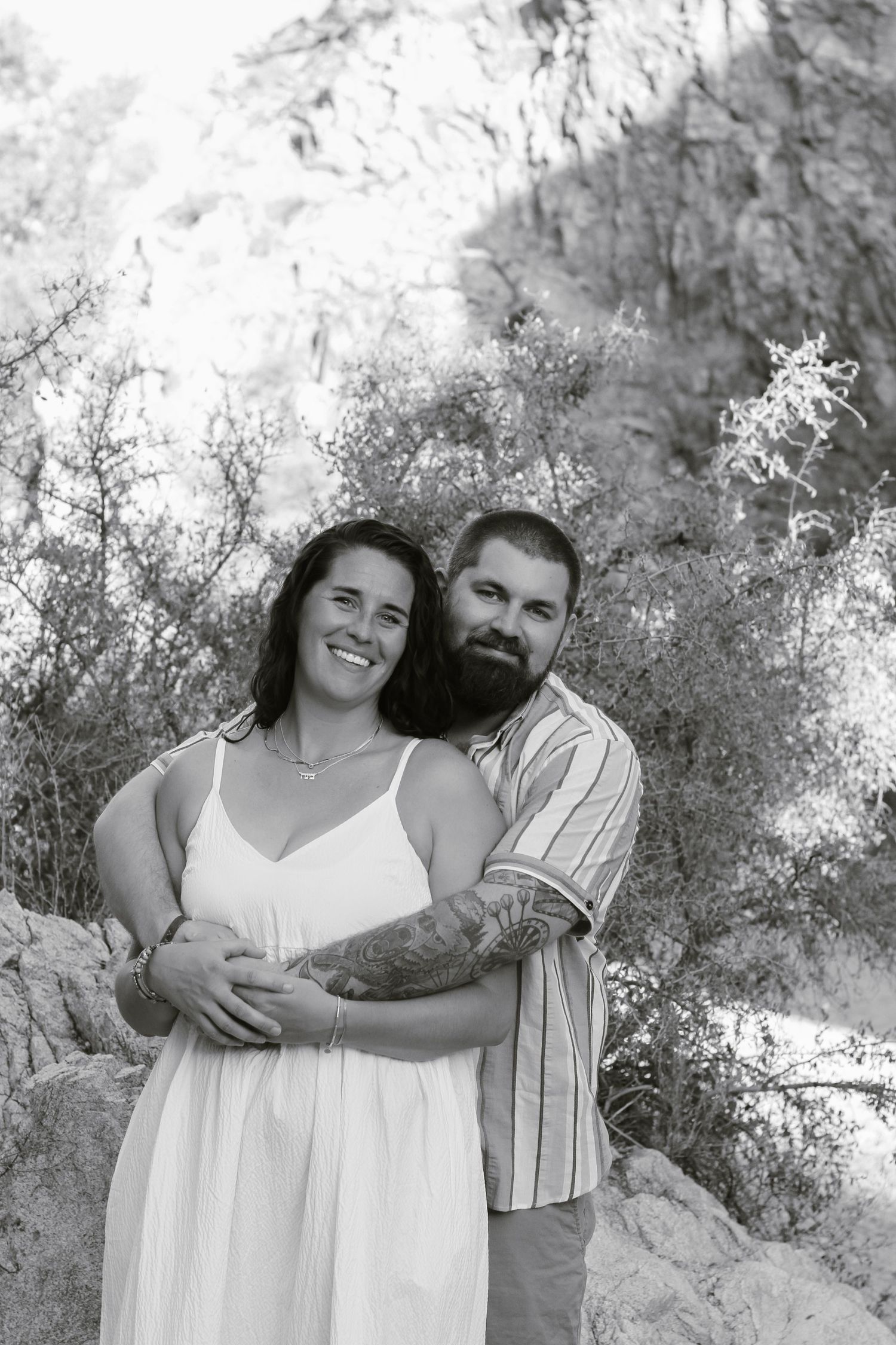 A black and white portrait captures a couple's joyful embrace outdoors.
