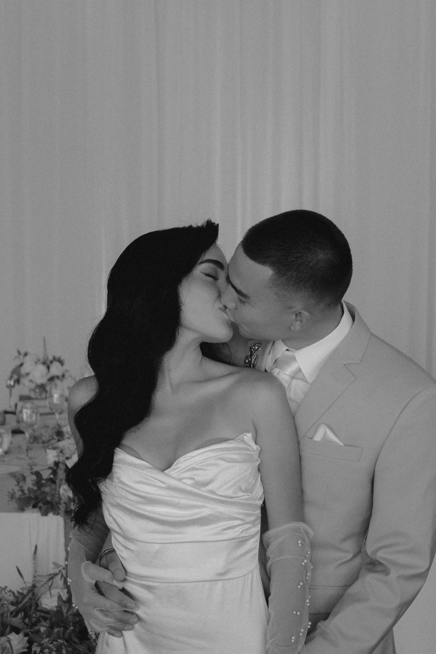 Black and white photo of bride and groom sharing a romantic kiss at their wedding ceremony.