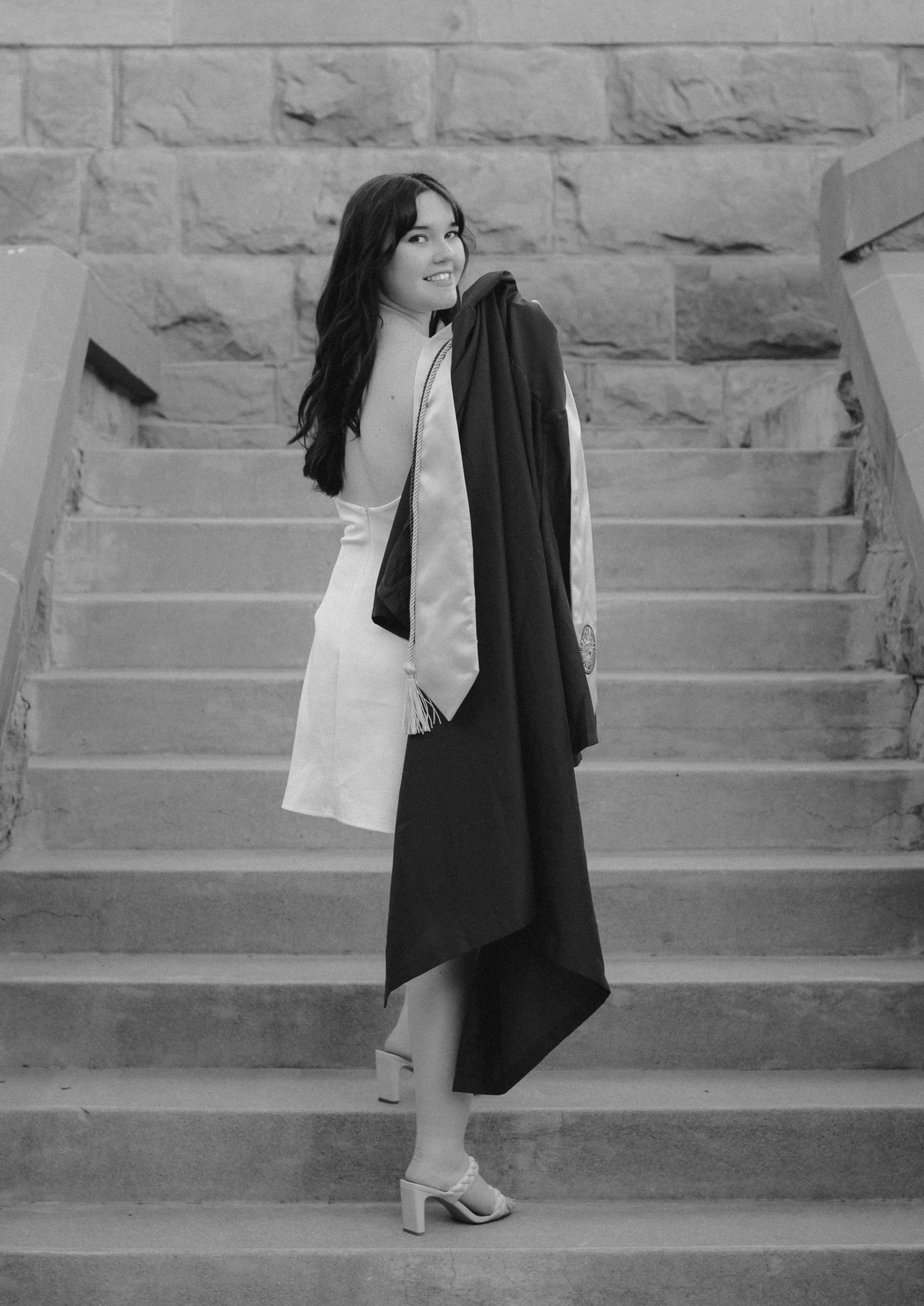 Graduate posing on stone steps in formal attire and graduation gown.