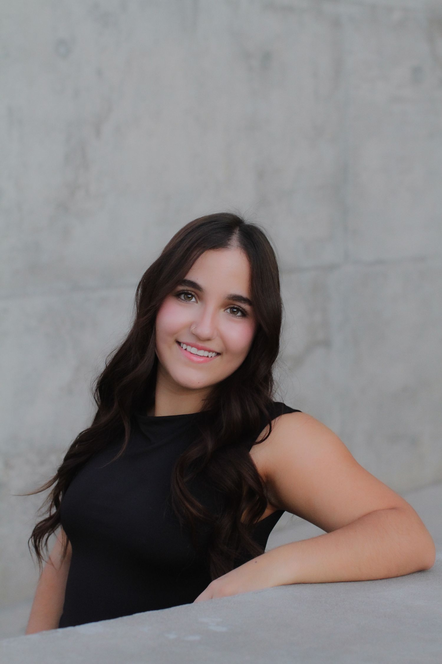 Portrait photo of someone in a black sleeveless top against a grey backdrop with a warm smile.