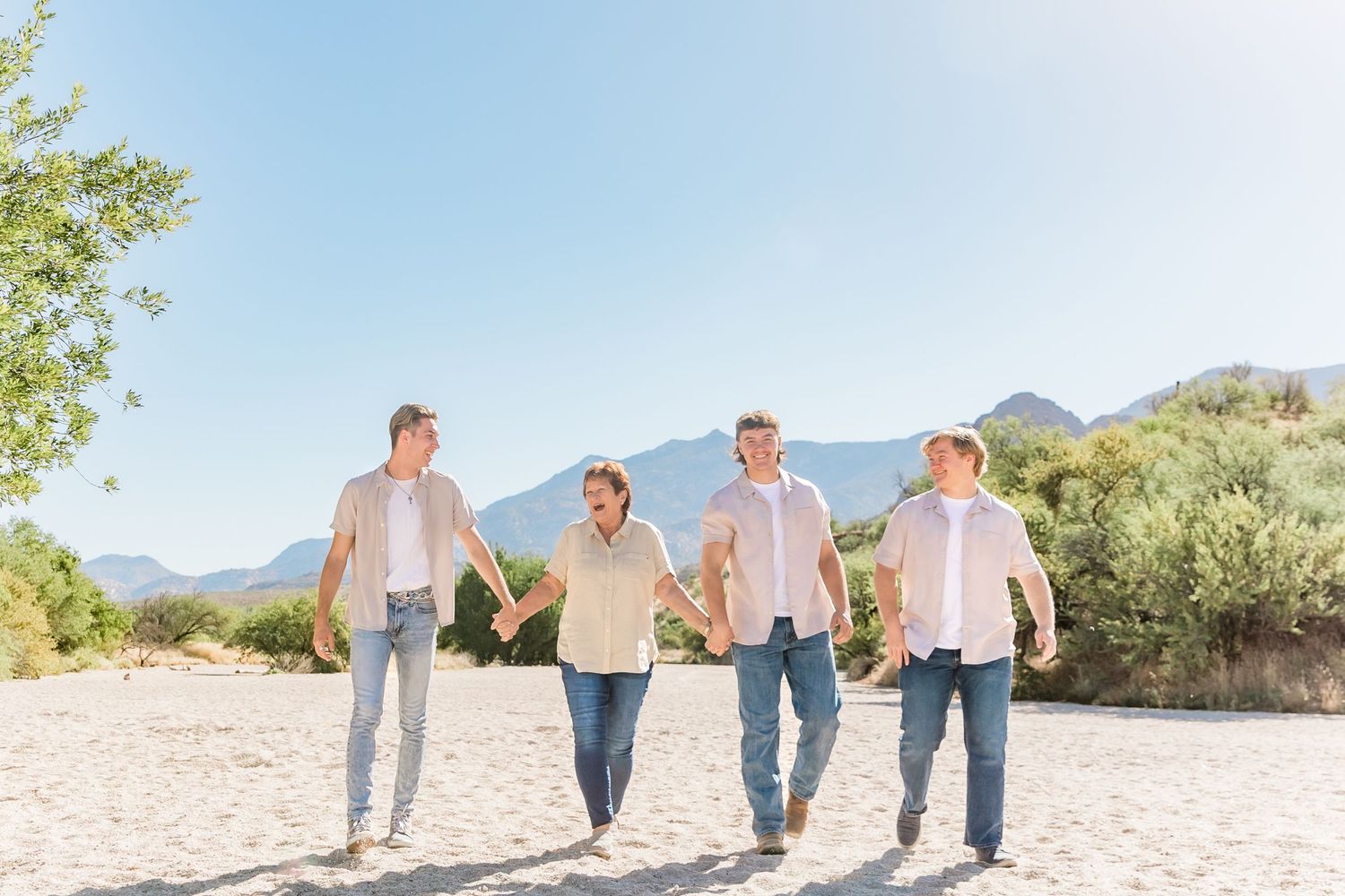 Four people walking together on desert path with mountains in background.