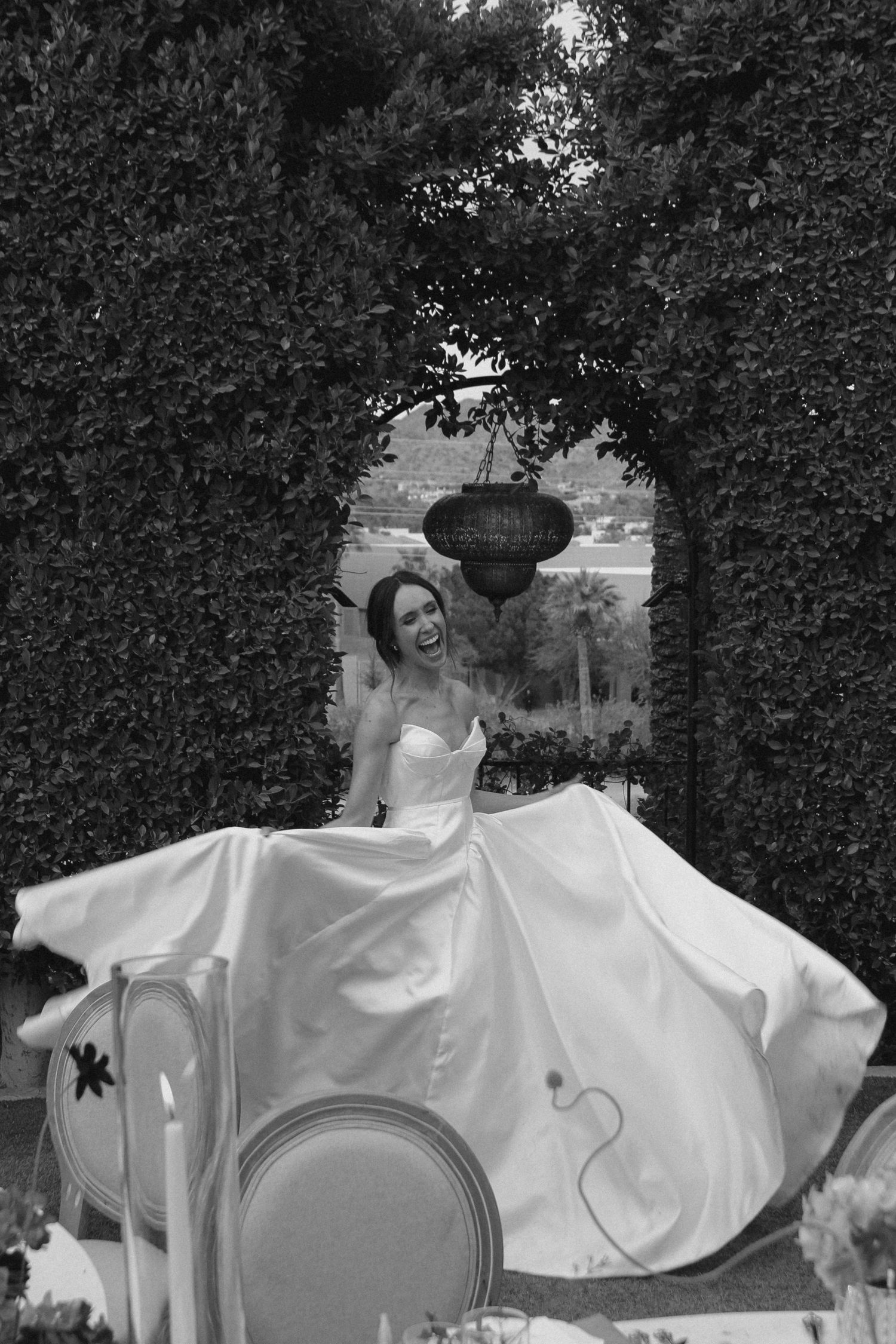 Bride in strapless ball gown twirling joyfully under a garden archway of lush greenery.