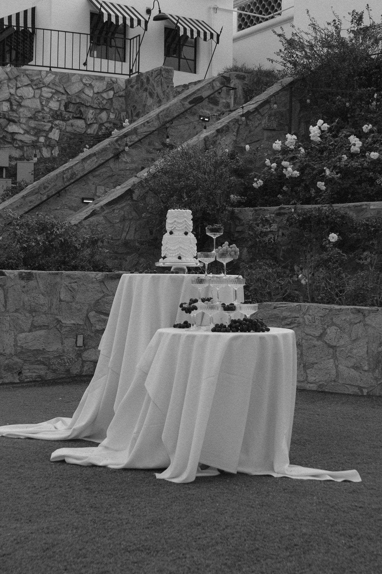 Black and white photo of an elegant tiered wedding cake display on white tablecloths.