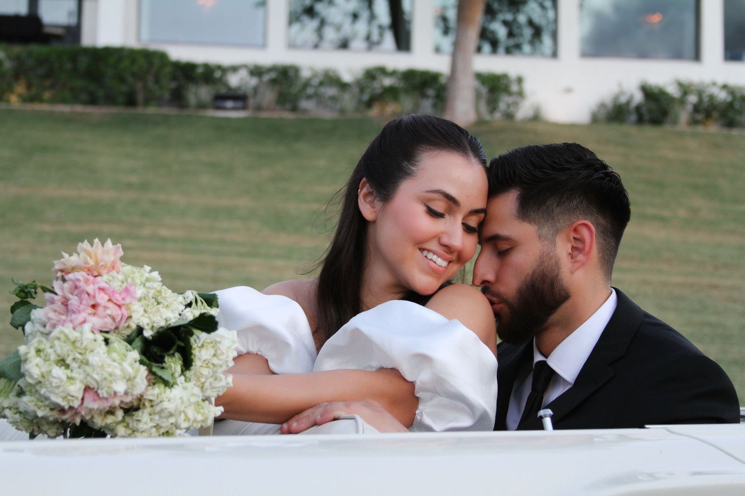 A romantic moment between newlyweds with a pink and white floral bouquet in the foreground.