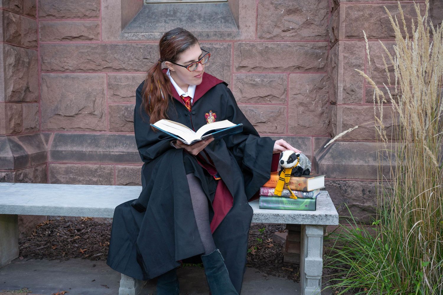 A woman dressed as a Hogwarts student from Harry Potter reading a book.