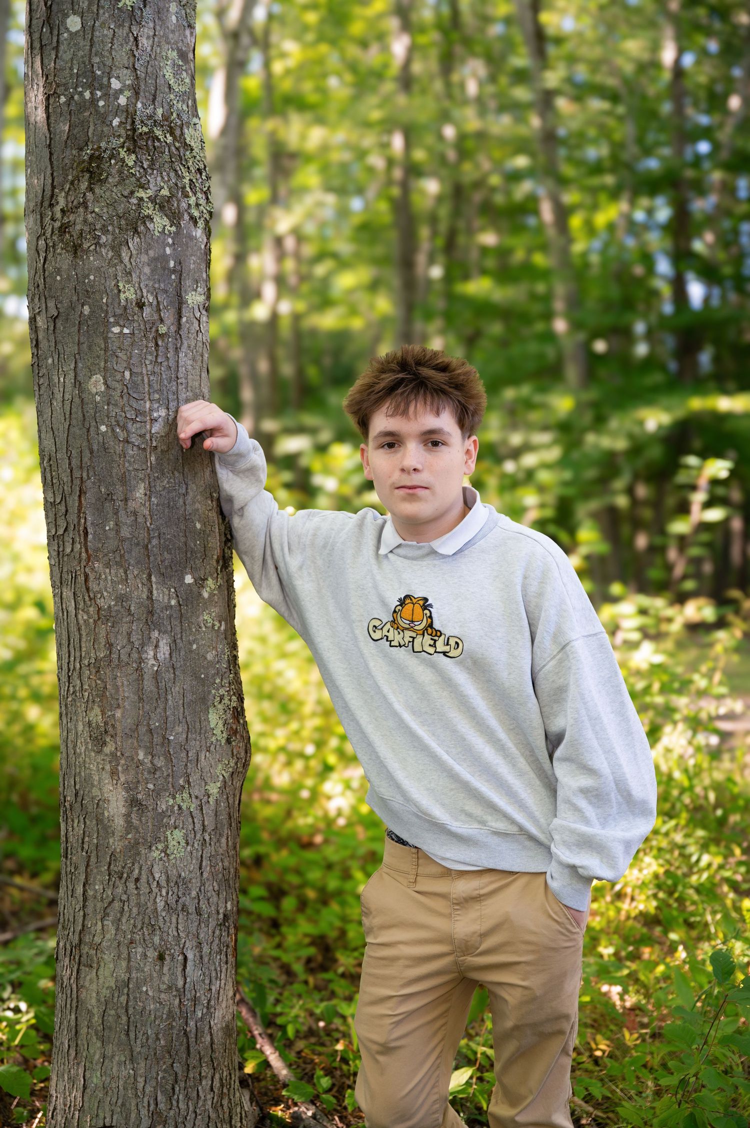 A high school senior poses next to a tree in the woods of Keene, New Hampshire.