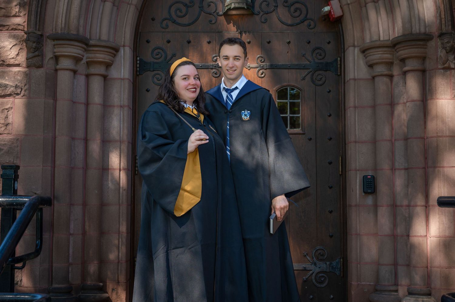 A couple standing together dressed in Harry Potter robes from Hufflepuff and Ravenclaw houses.