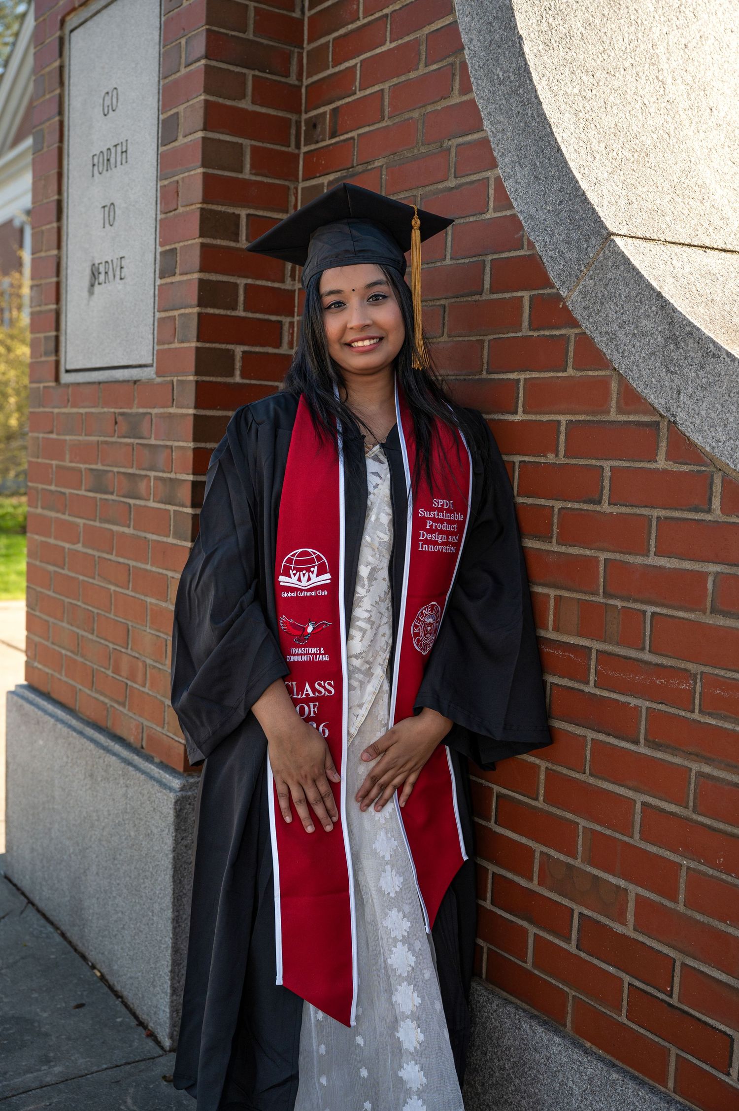A Keene State College graduate poses for a true to color photo in a cap & gown.