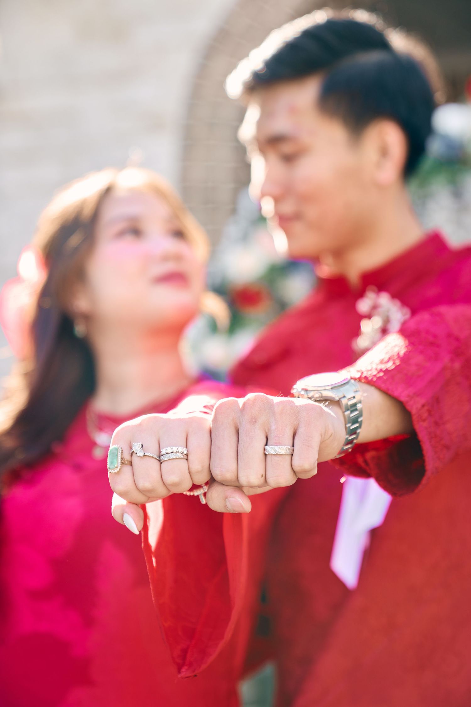 Asian couple in traditional red attire show off their wedding rings together in romantic engagement photo.