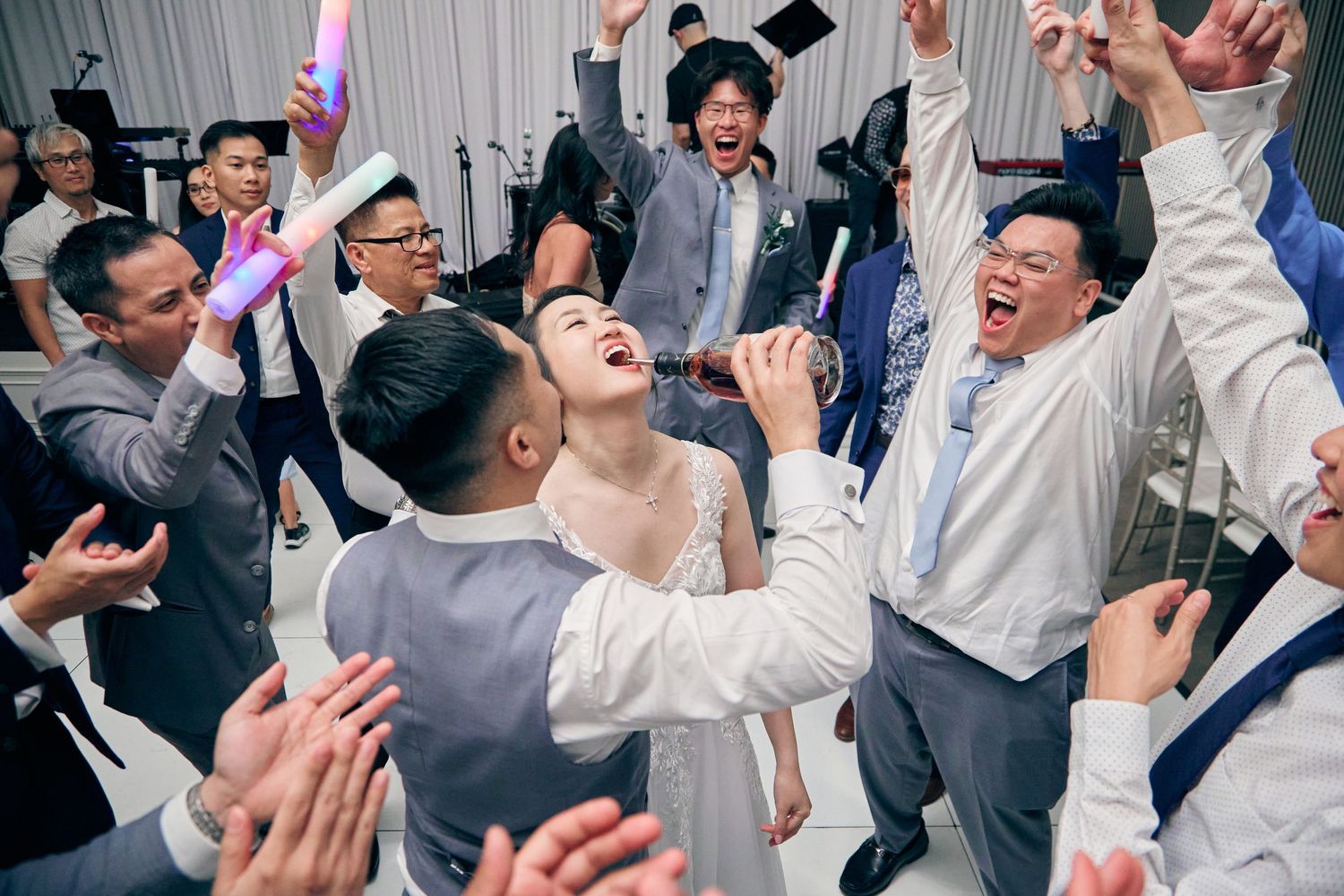 Joyful wedding reception dance floor celebration with bride and groom surrounded by cheering guests.