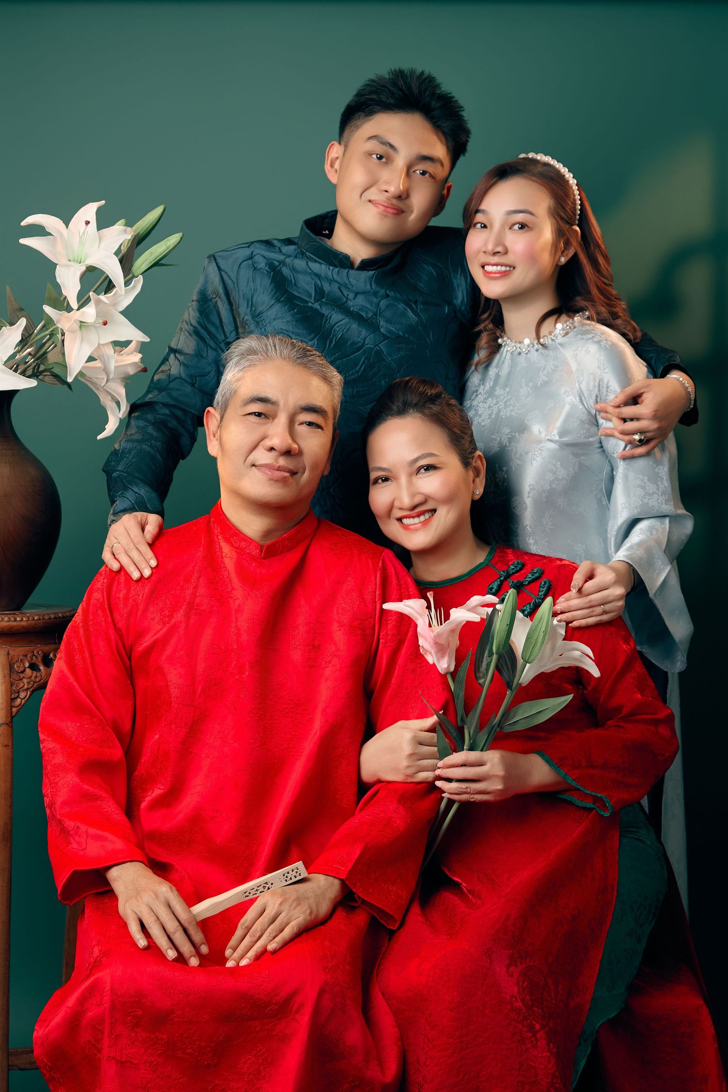 A Vietnamese family of four poses elegantly in traditional red and blue ao dai attire with lily flowers.