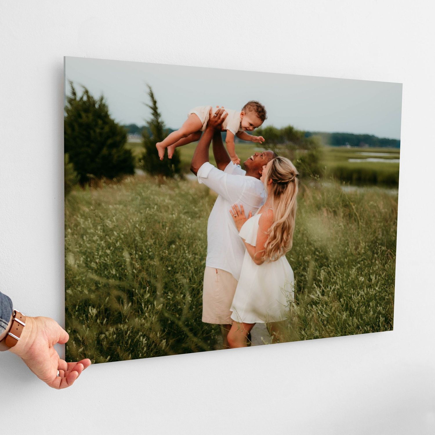 Family photo canvas print showing parents lifting baby in a green meadow landscape.