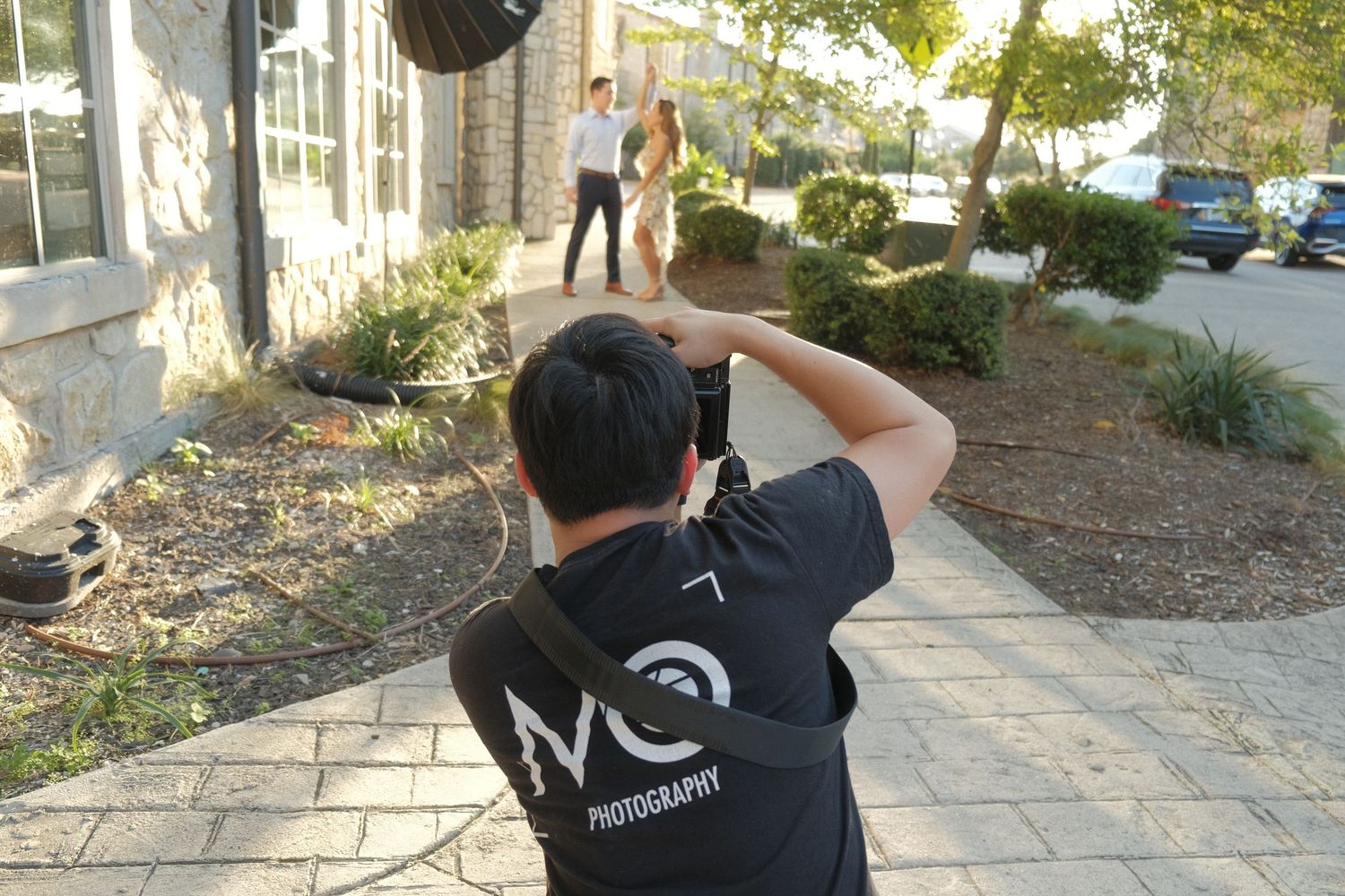Wedding photographer capturing couple outdoors during a sunny day photo session.