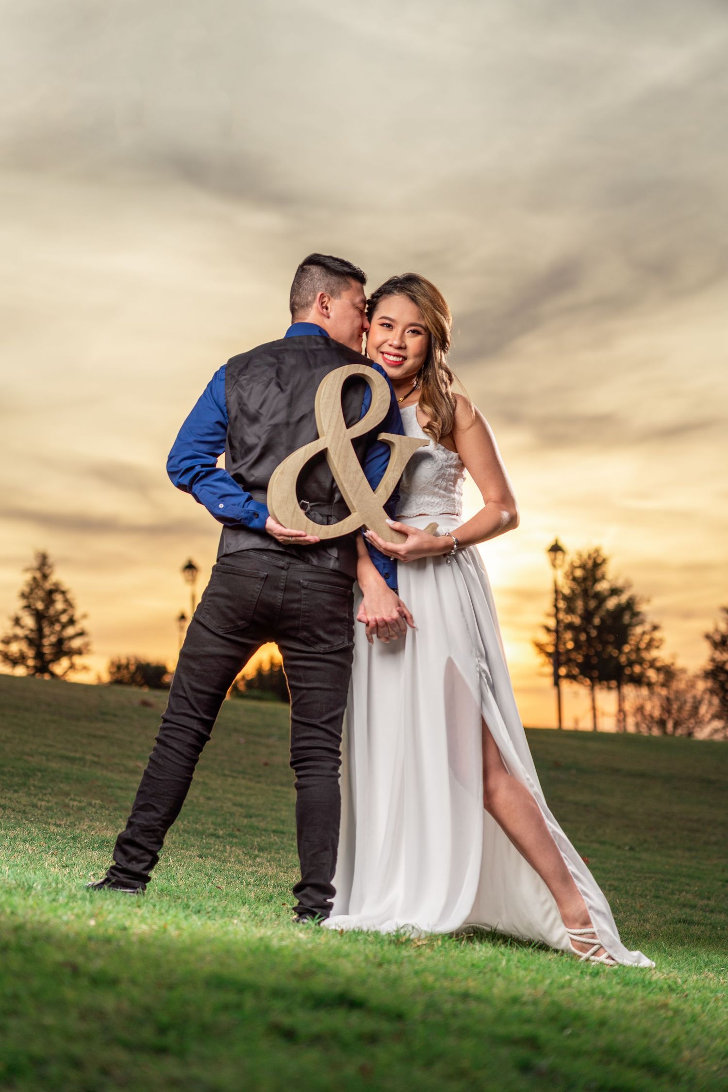 Happy couple holding an ampersand sign at sunset in a lush green park.