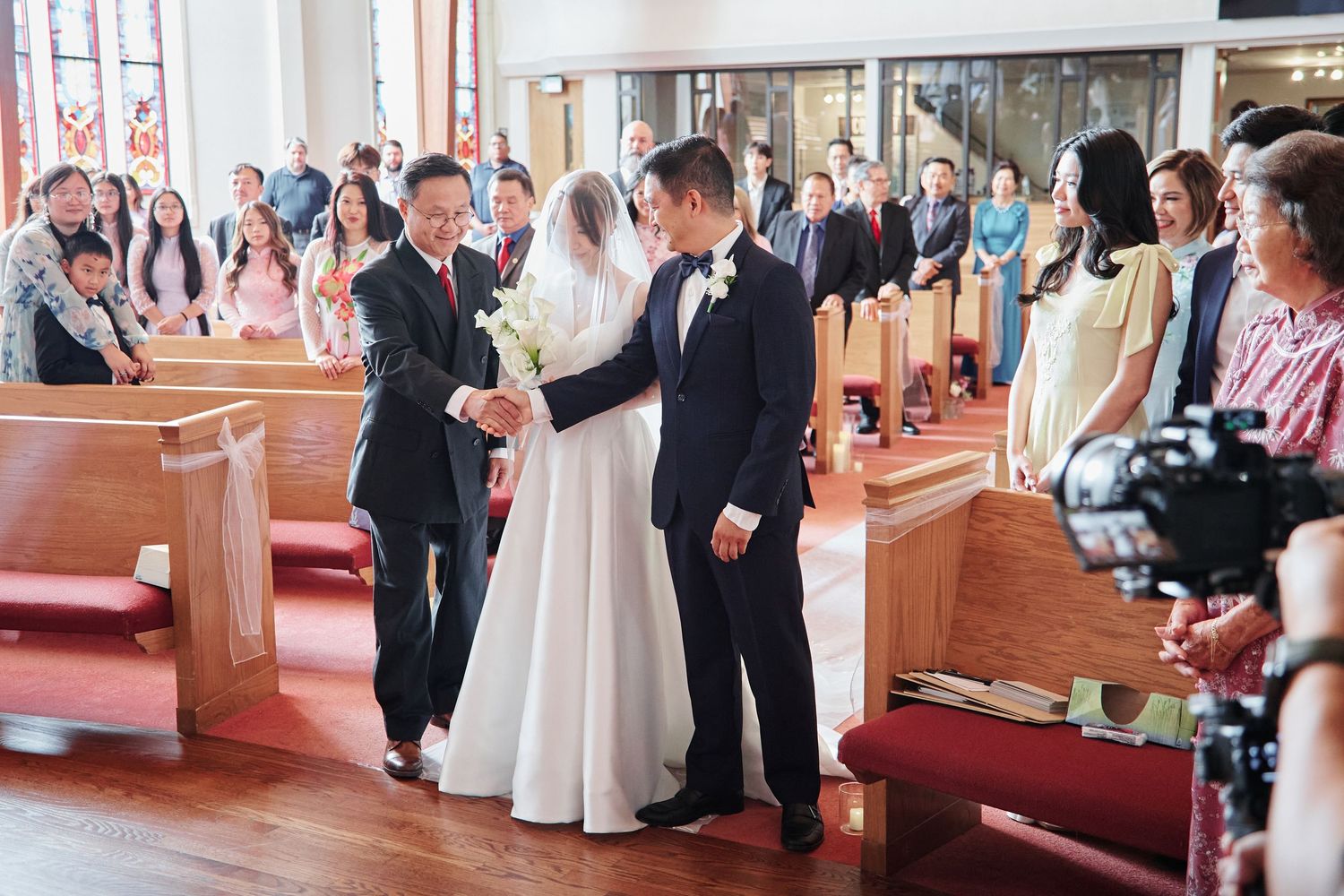 Wedding ceremony moment as father hands bride to groom at church altar with guests watching.