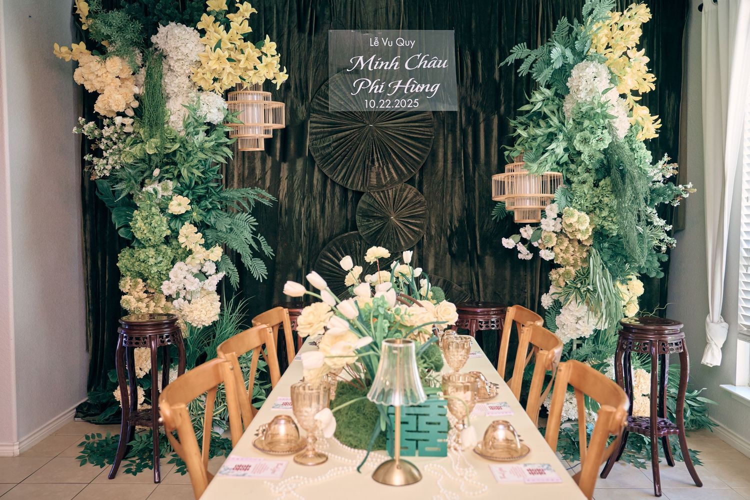 Elegant Vietnamese wedding reception table decorated with lush greenery, yellow flowers, lanterns, and a personalized sign.