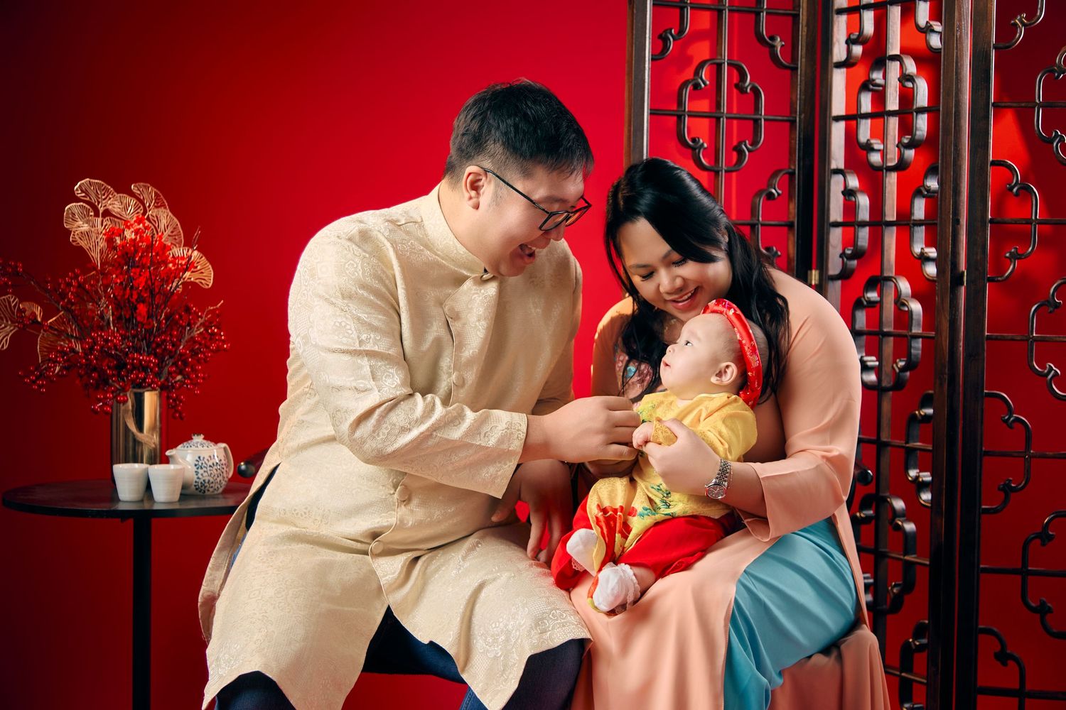 Asian couple in traditional golden outfits celebrating with their baby dressed in festive red attire.