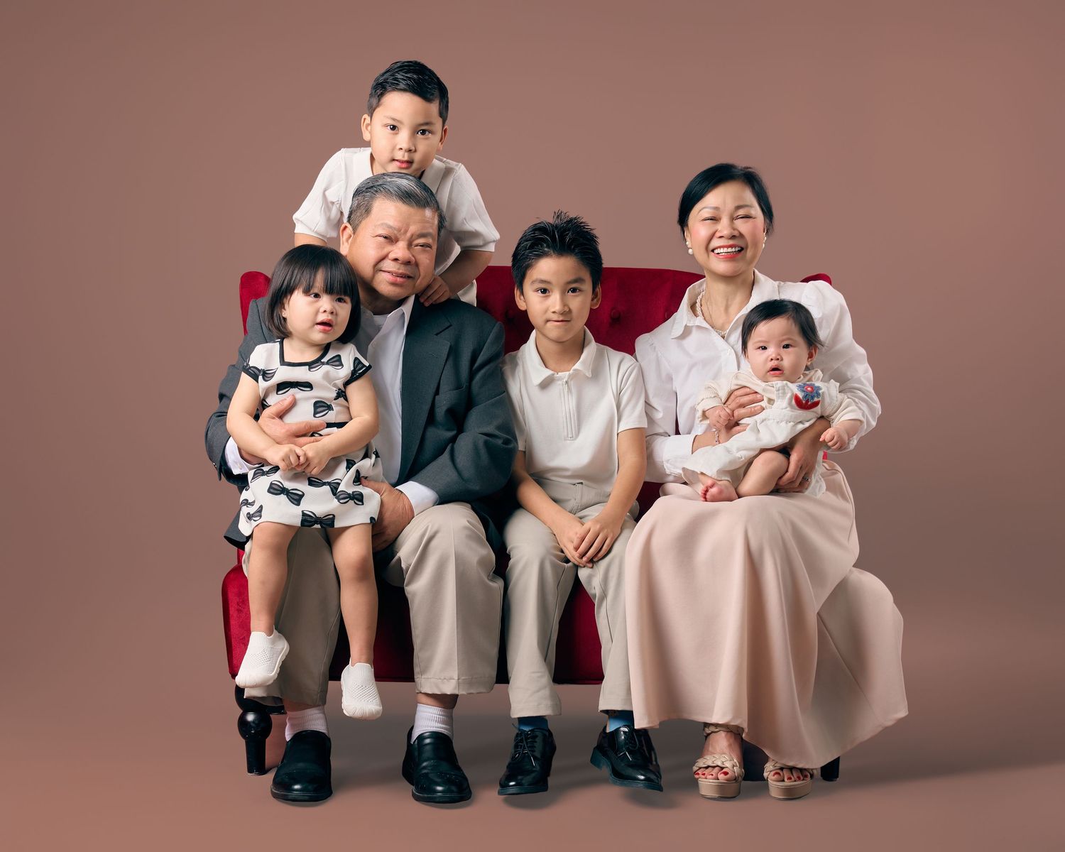 Grandparents seated on red sofa surrounded by four grandchildren in warm studio family portrait.