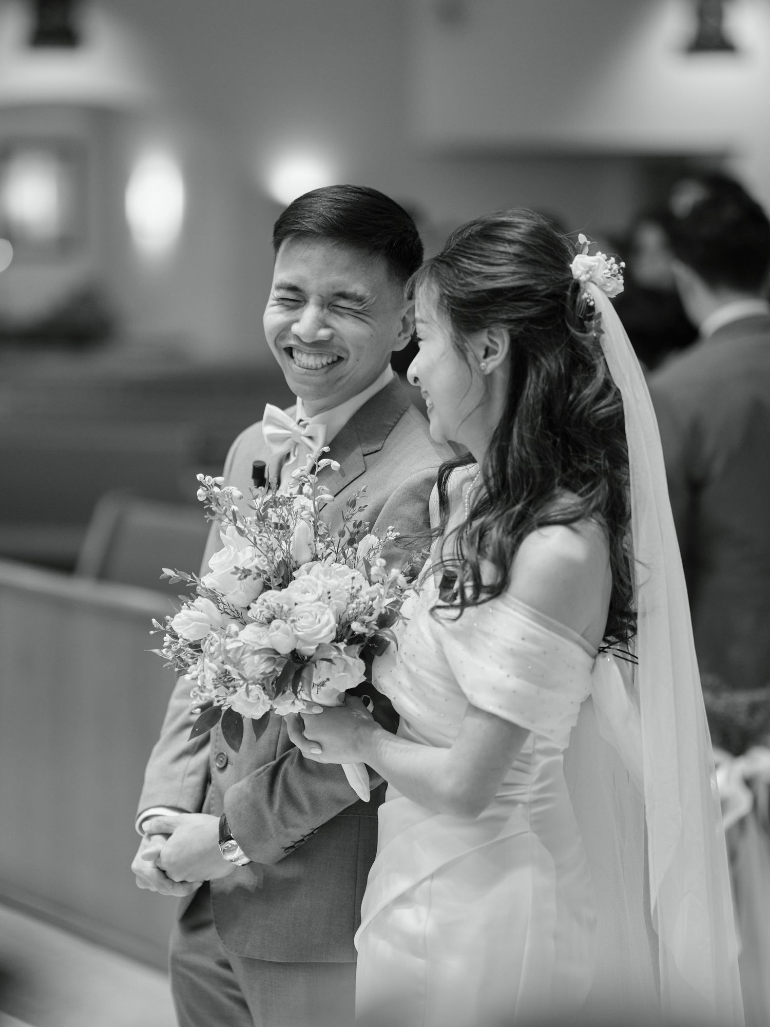 Smiling groom and bride sharing a joyful moment at the church altar in black and white.