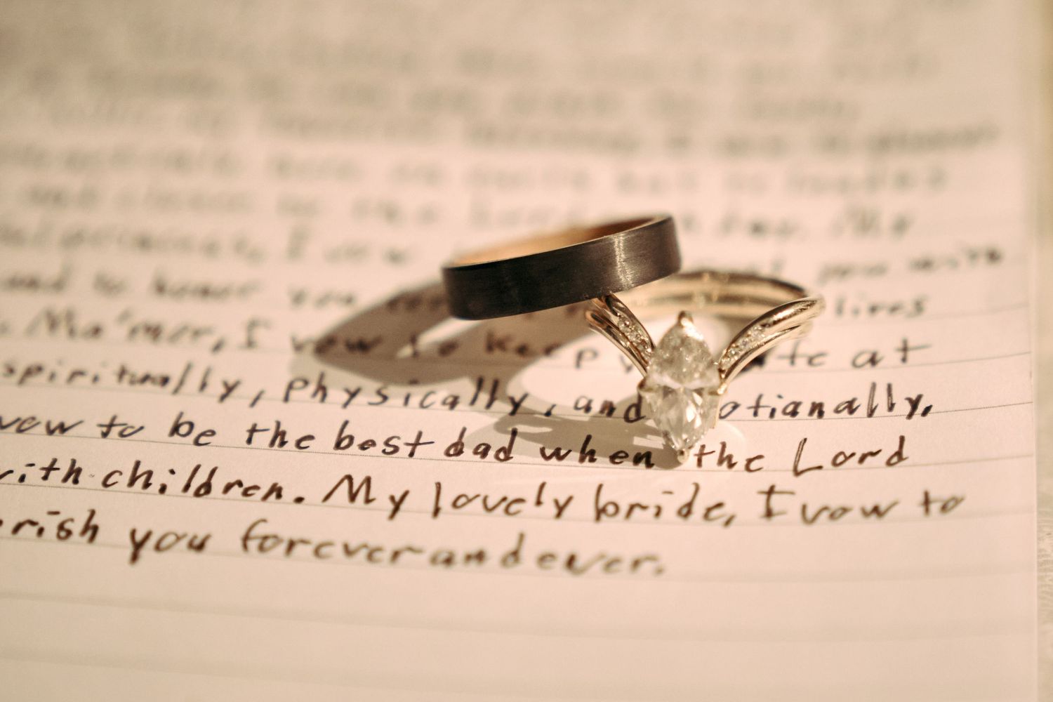 Wedding rings resting on handwritten vows letter with diamond engagement ring and gold band close-up.