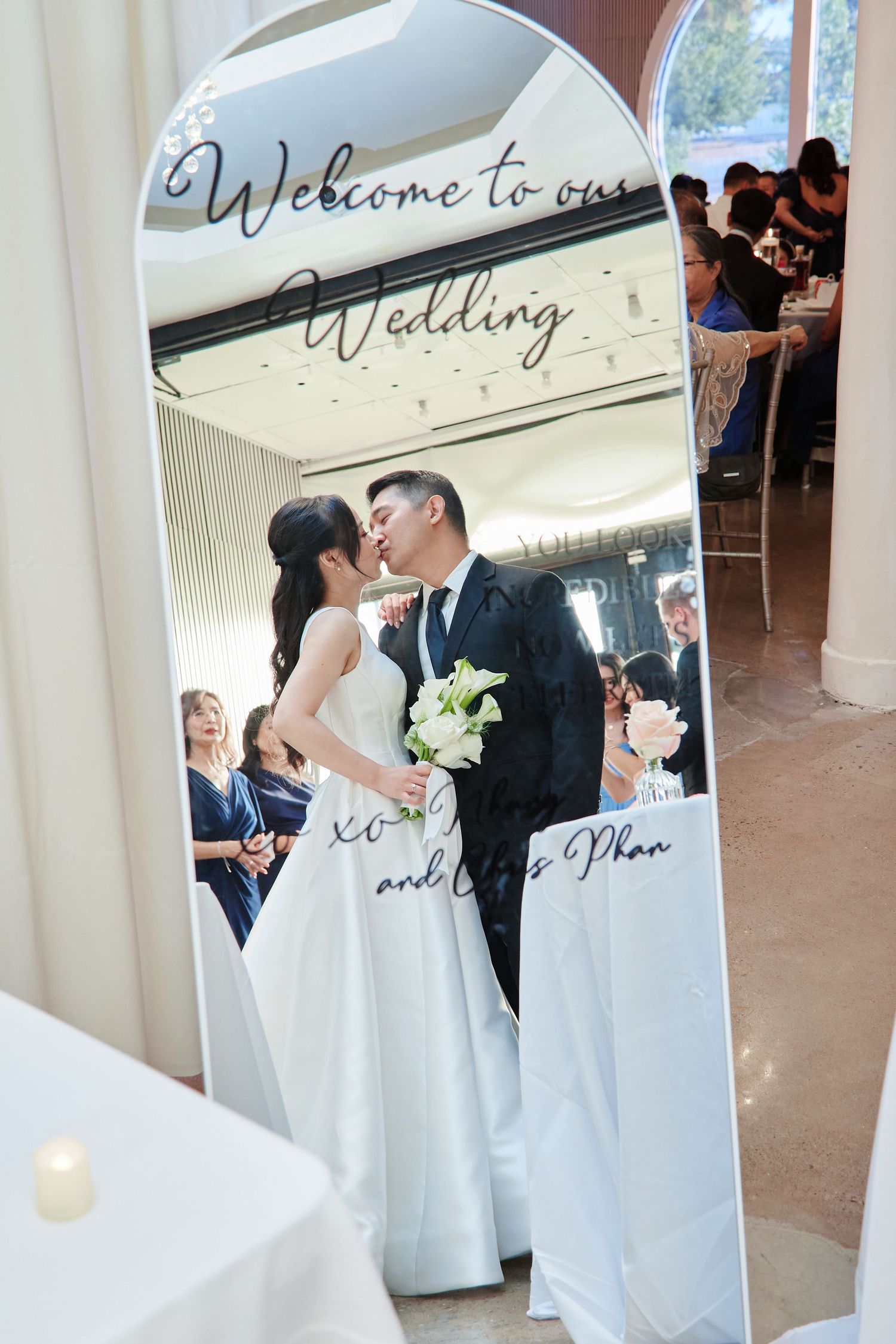 Bride and groom share a kiss reflected in an elegant welcome wedding mirror sign.