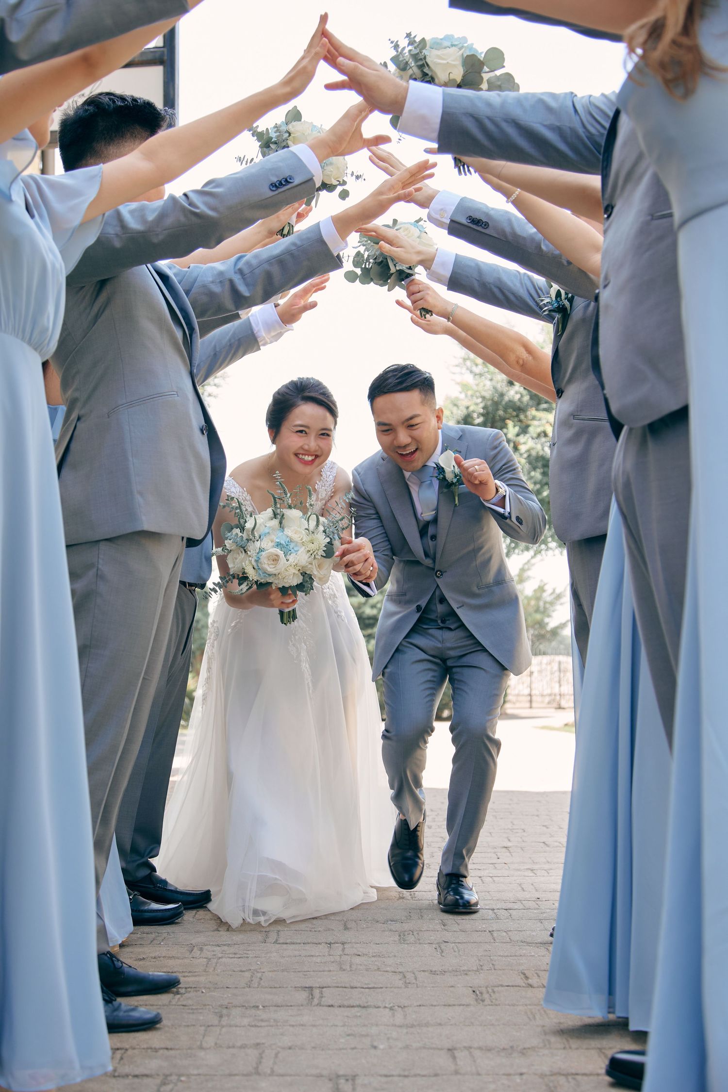 Laughing newlyweds run through an arch of raised hands formed by bridesmaids and groomsmen.