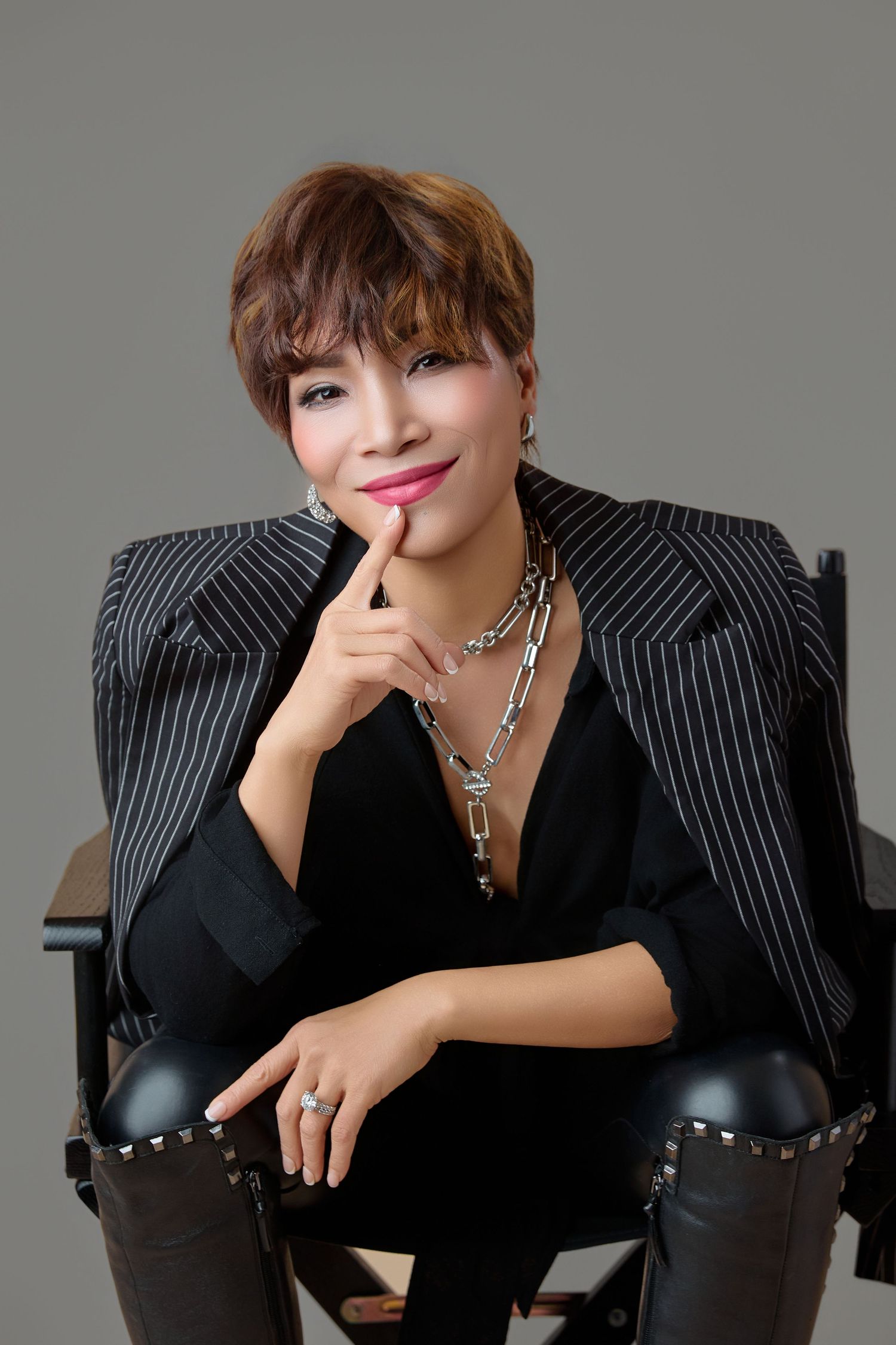 Confident Asian woman in pinstripe blazer sitting in director chair with thoughtful pose.