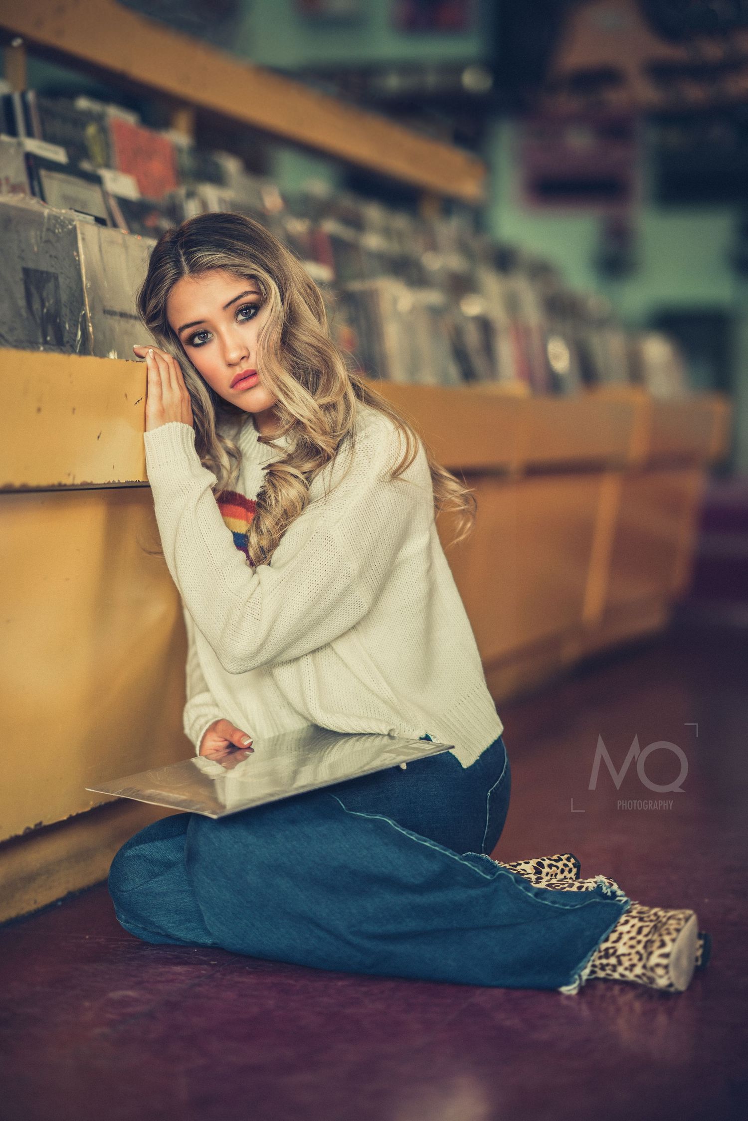 Blonde woman in cream sweater sitting on floor of vintage vinyl record store.